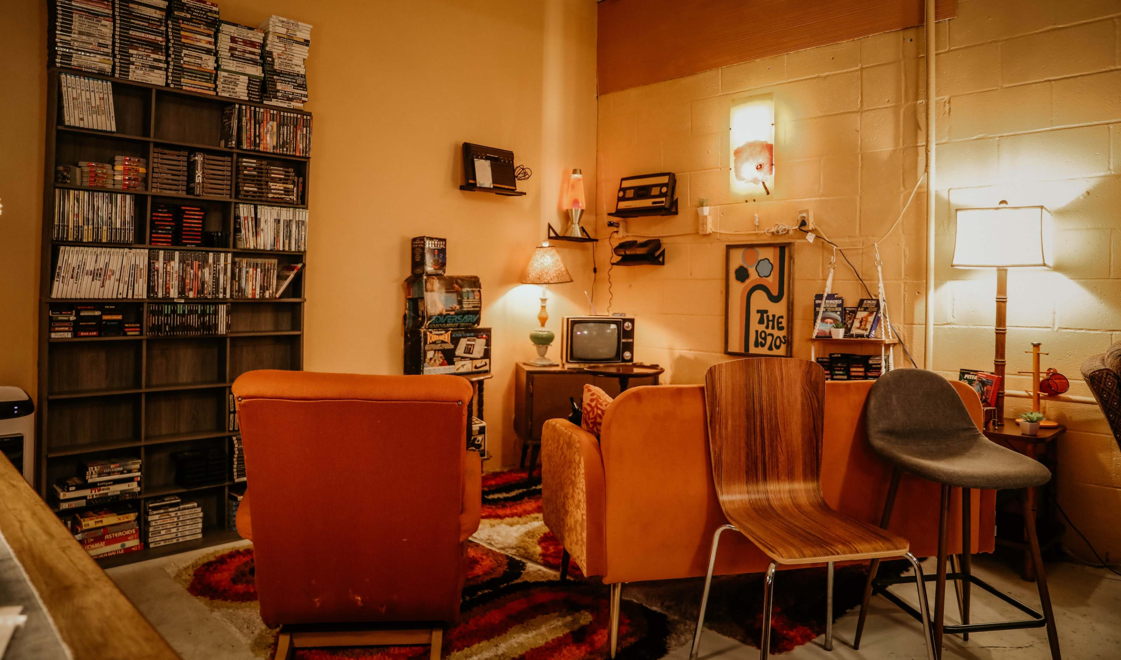 A retro-themed living room with a collection of video games on a shelf, vintage furniture, and a small television set.