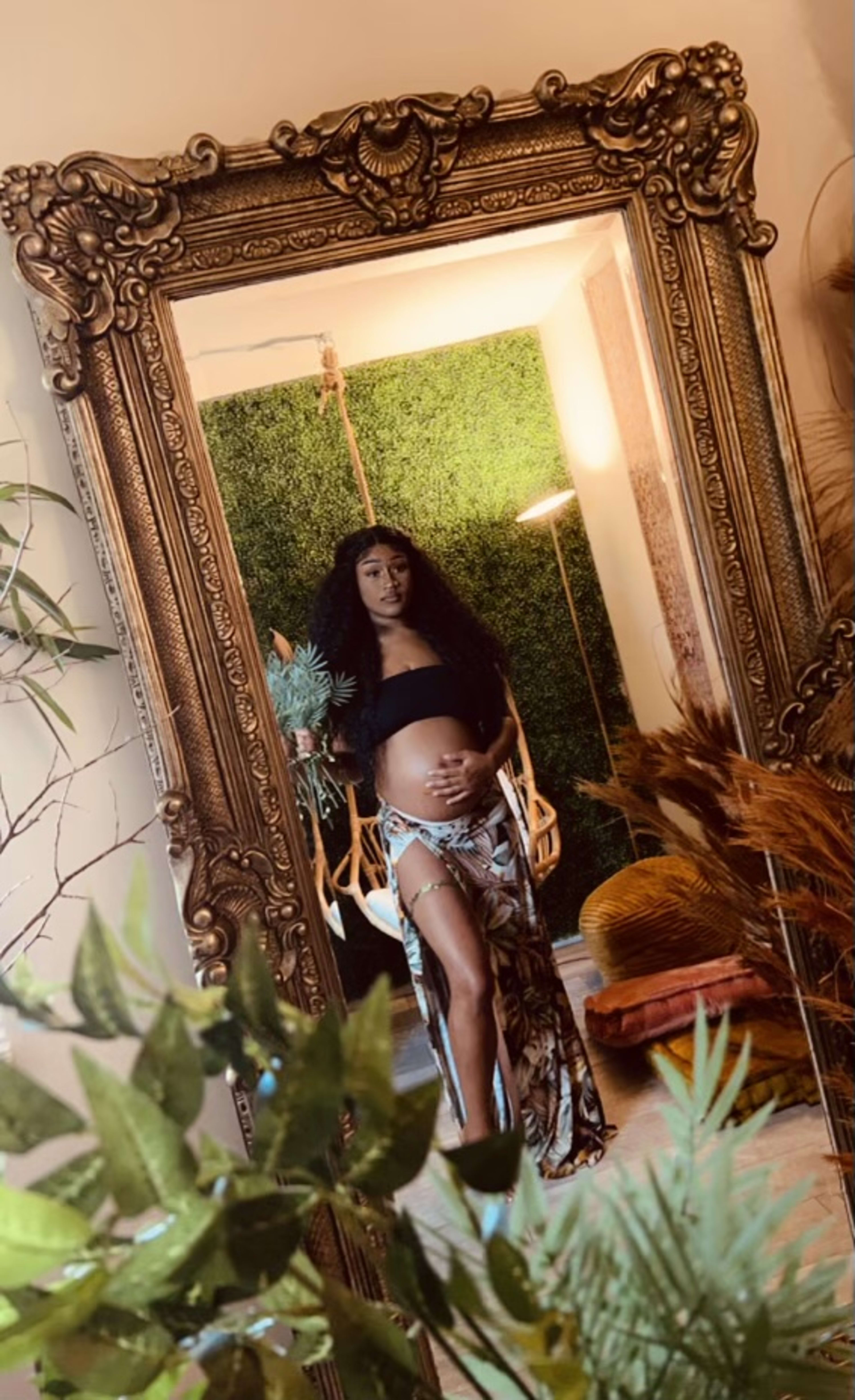 A pregnant woman standing in front of a mirror in a boho setting