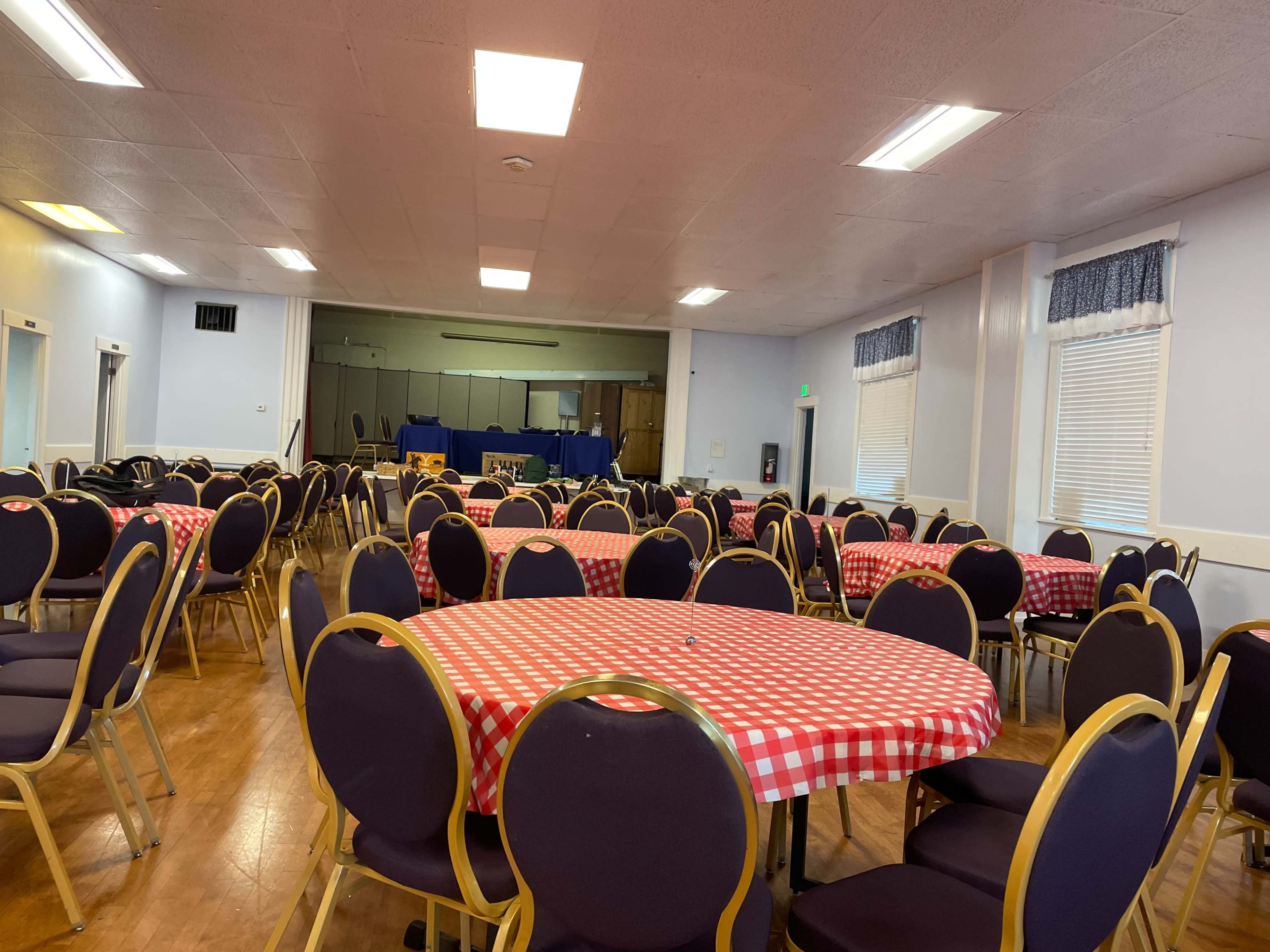 A spacious room filled with round tables covered in red-and-white checkered tablecloths, arranged for a gathering or event.