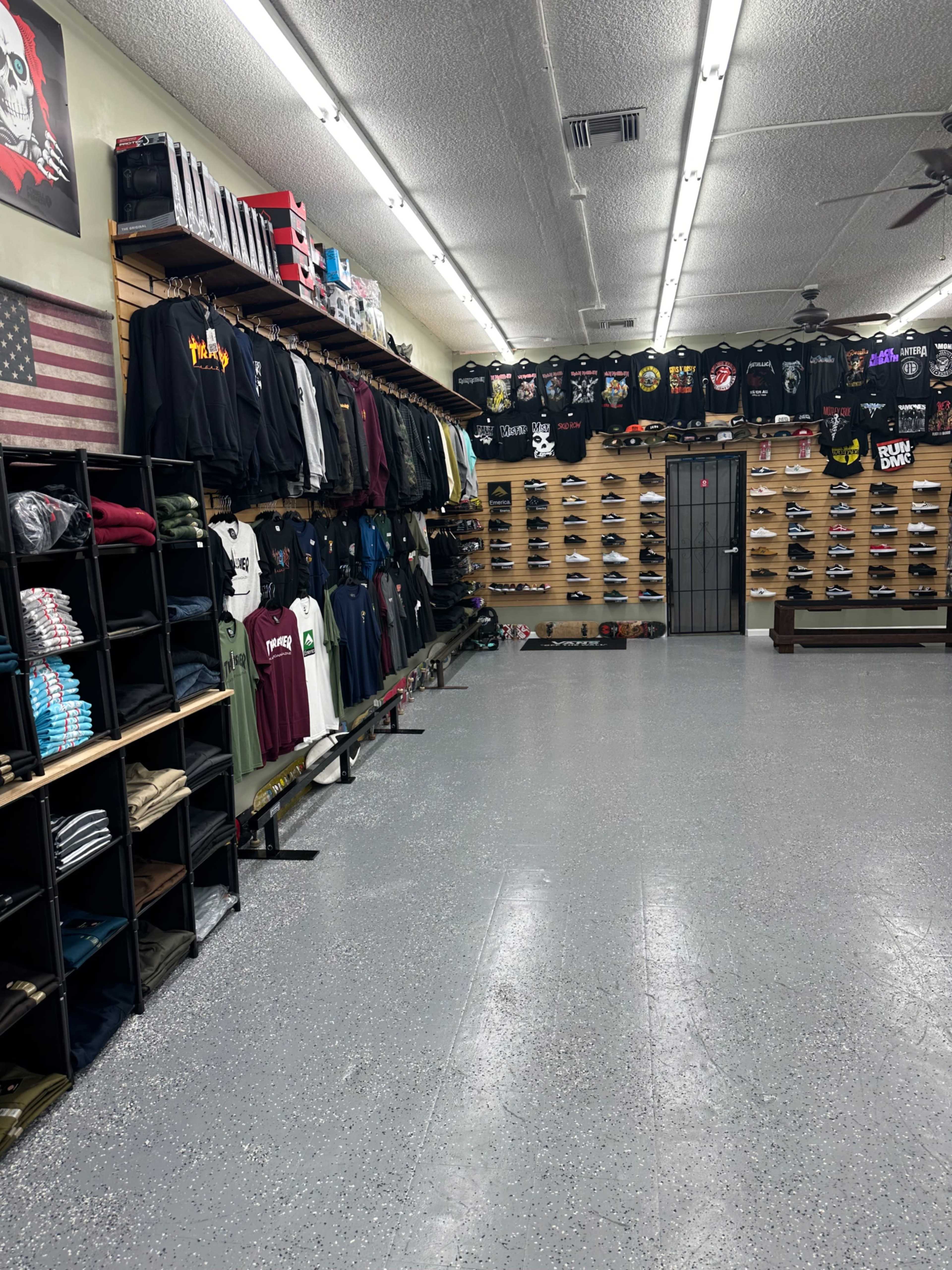 The interior of a retail store displays clothing on racks and shelves, with a wall of t-shirts and various apparel on the right and a row of footwear on the left.