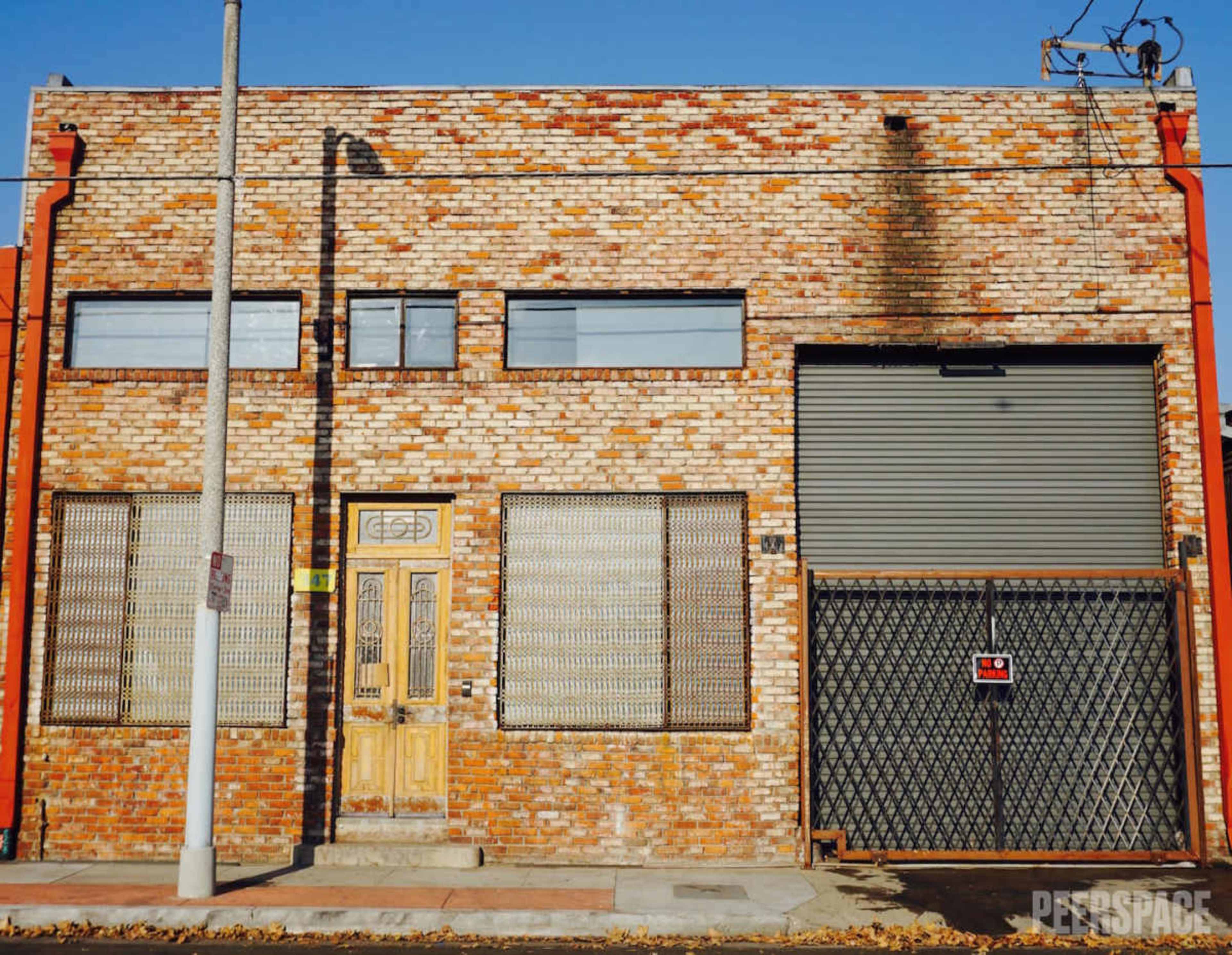 The image shows a brick building with a wooden door and metal security grates, located at street level with a clear blue sky above.