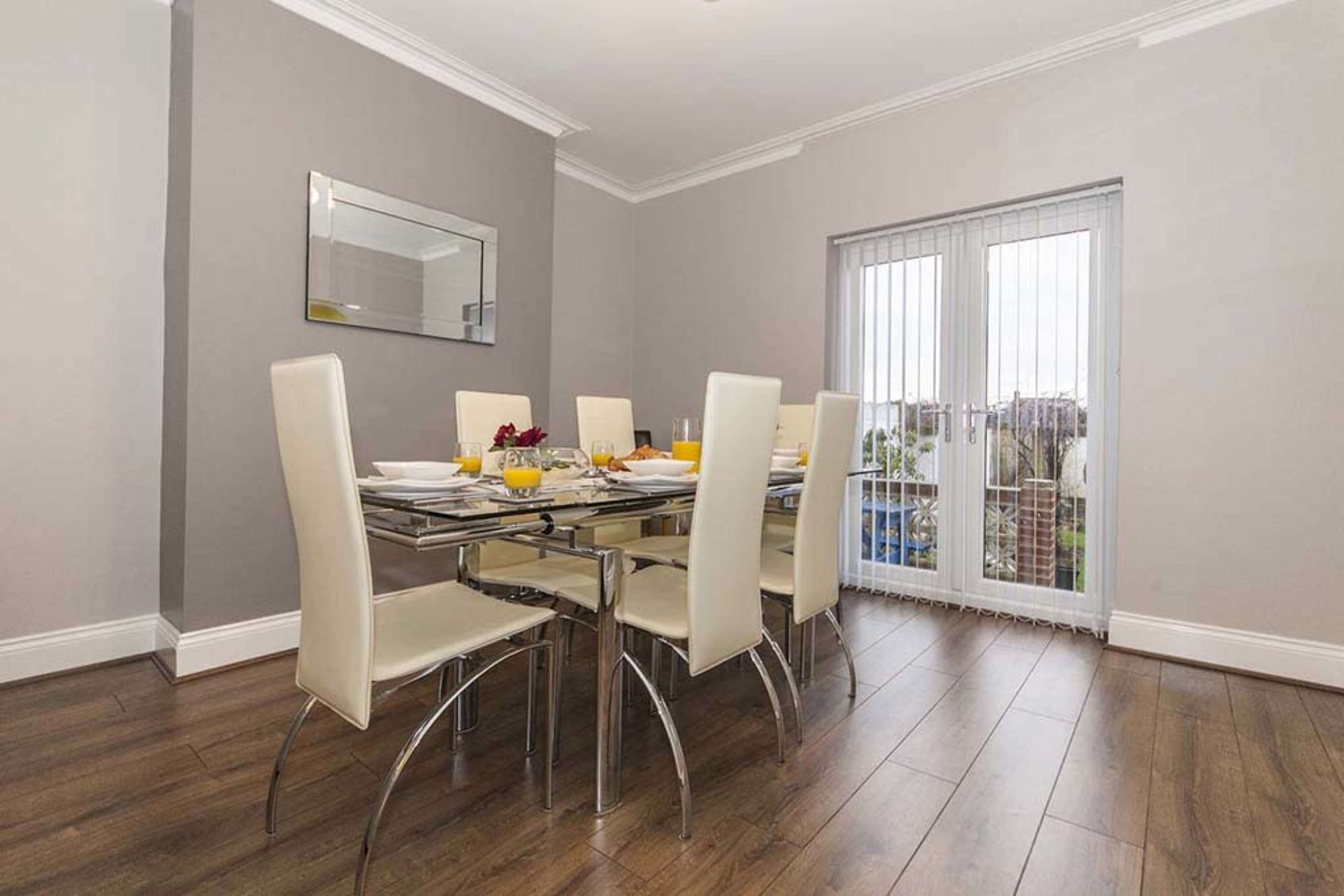 A modern dining area features a glass table with six light-colored chairs and a view through sliding glass doors.