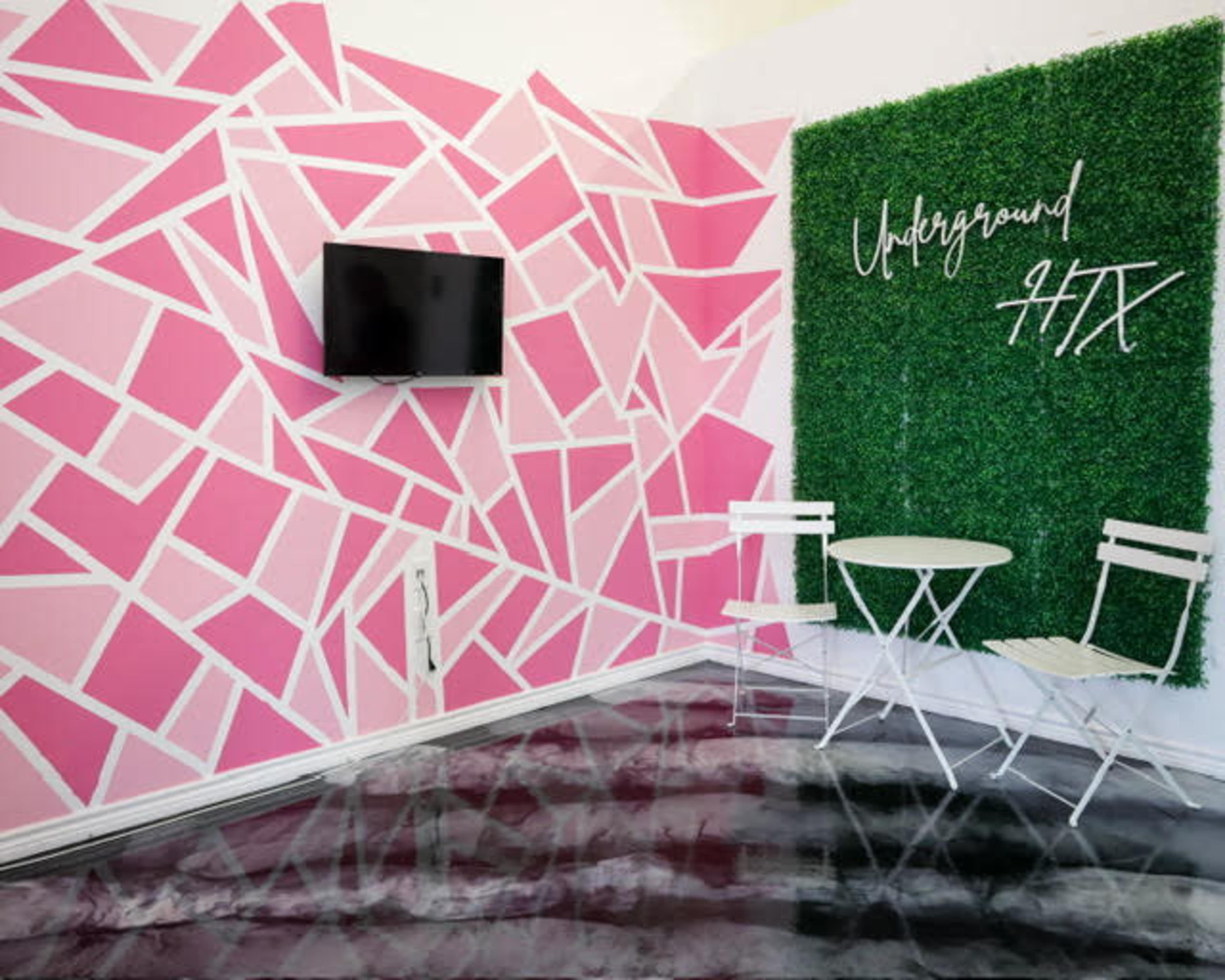 The room features pink geometric wall artwork, a green foliage accent wall with the text "Underground HTX," and a small white table with two chairs.