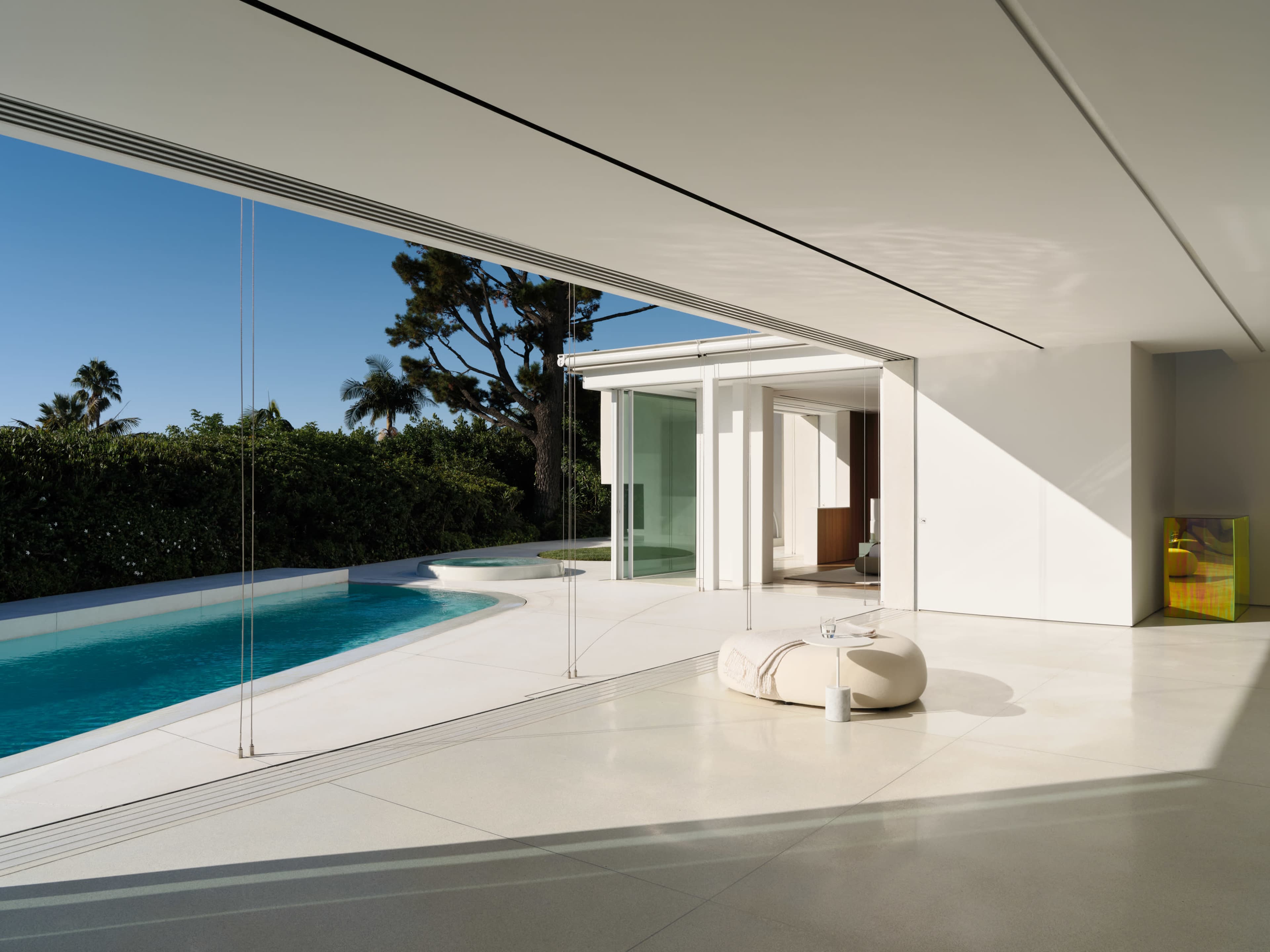 A modern interior space features large glass walls overlooking a pool and lush greenery.
