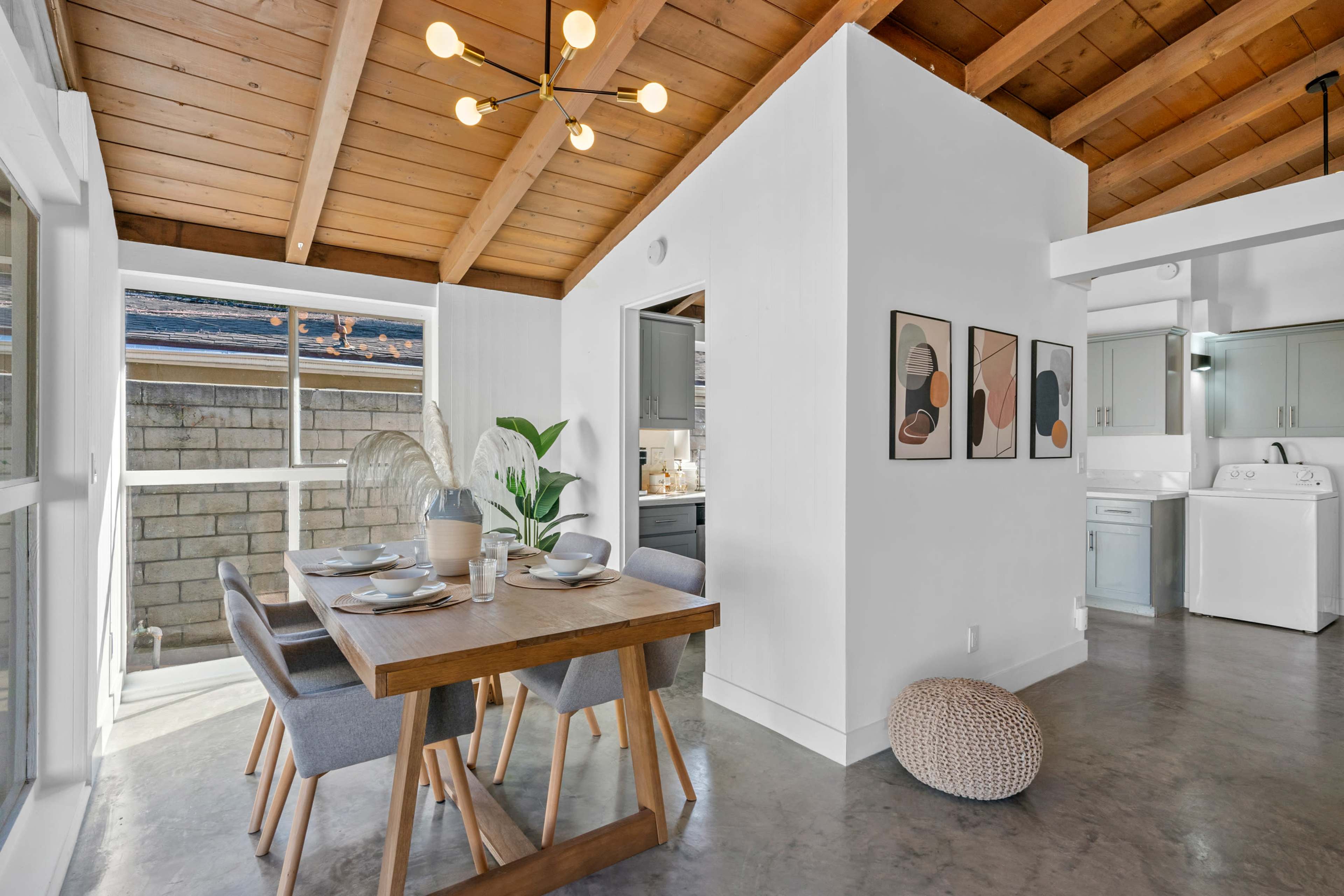 A modern kitchen and dining area featuring a wooden table with gray chairs, a ceiling light fixture, and light-colored walls.