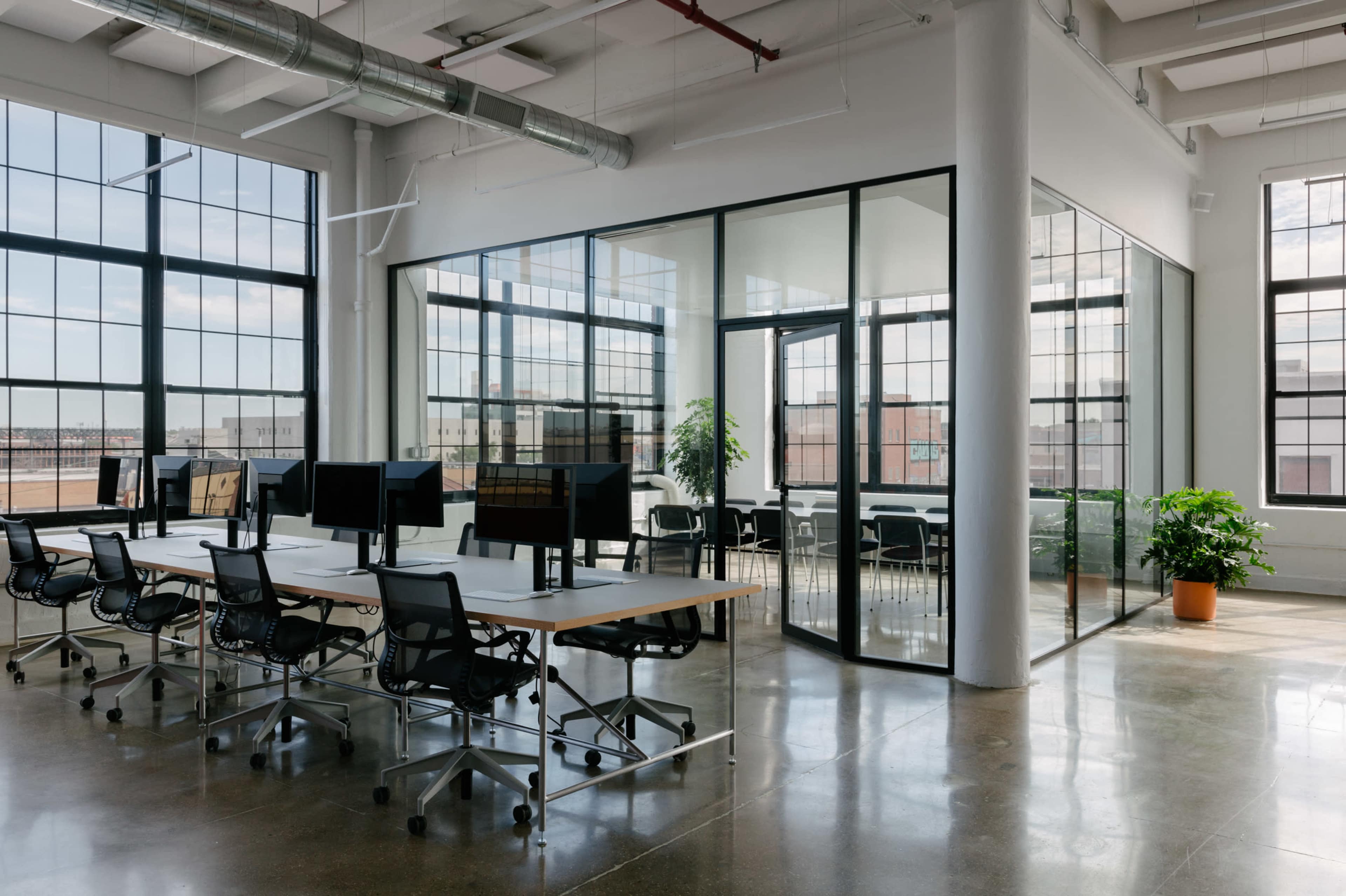 A modern office space featuring a row of desks with computer monitors and a glass-walled meeting room.
