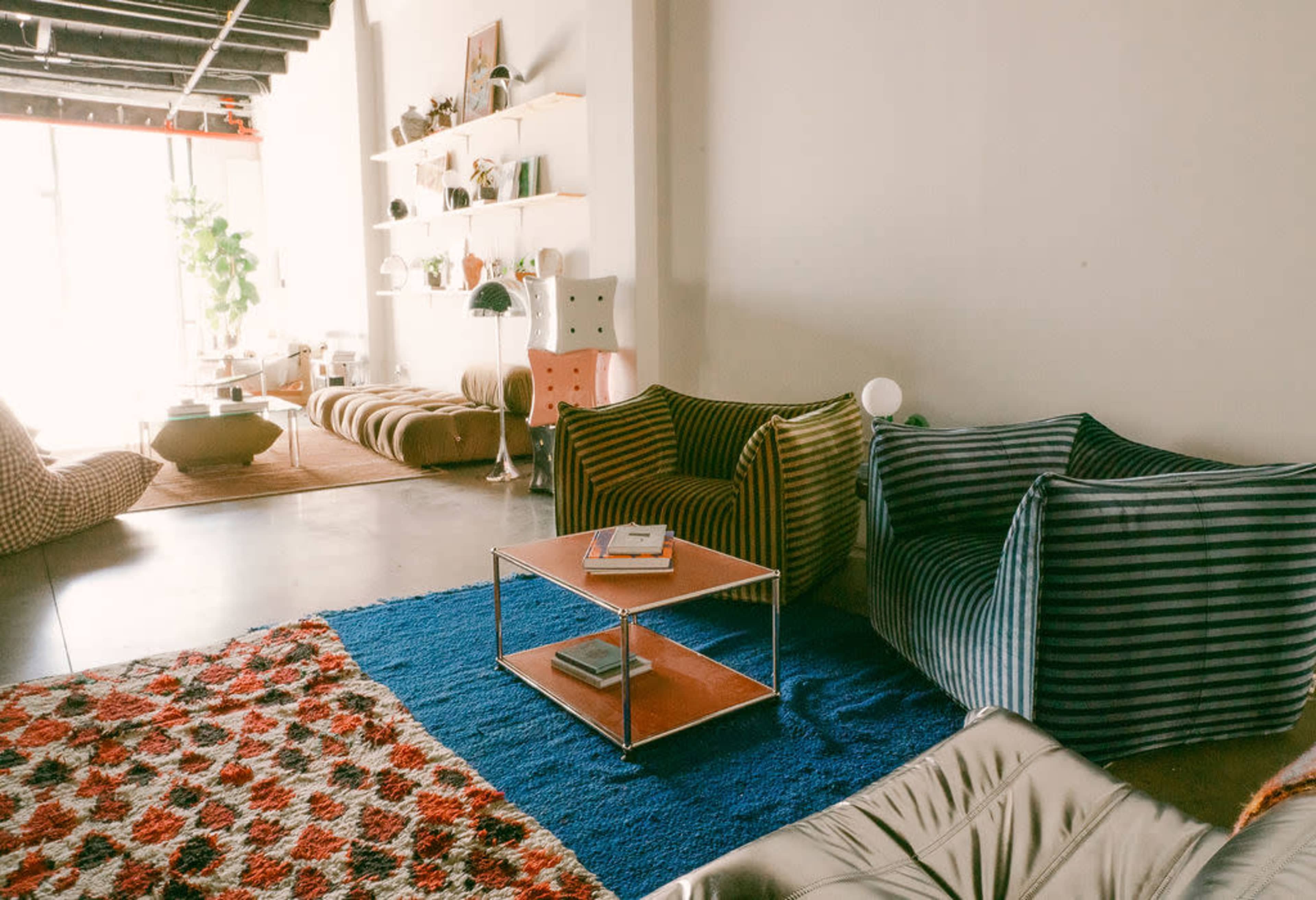 The scene features a modern interior with textured seating arrangements, a patterned rug, and a minimalist coffee table on a concrete floor.