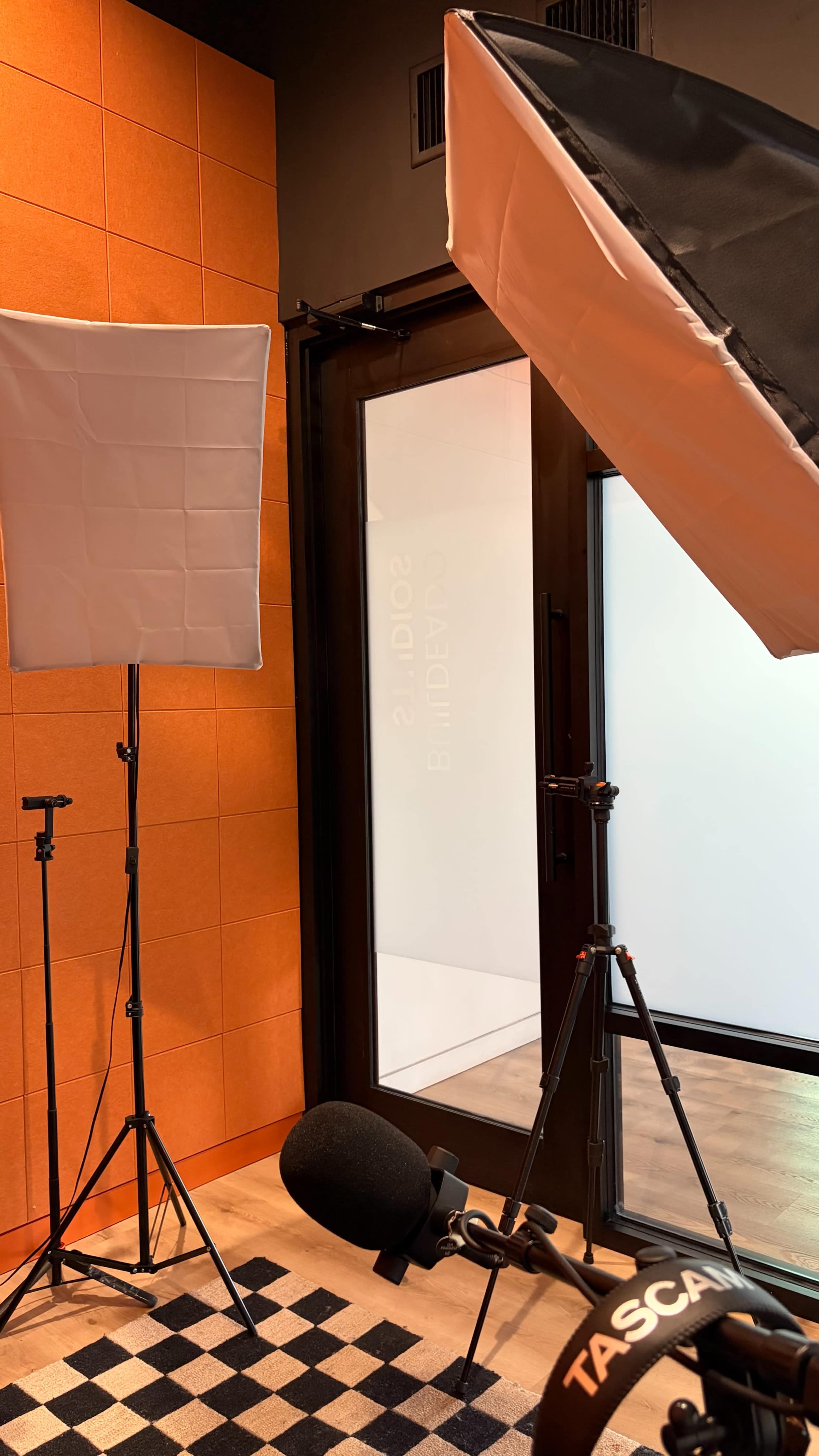 The image shows a room with orange walls and two lighting setups positioned on tripods near a glass door labeled "STUDIO 2."