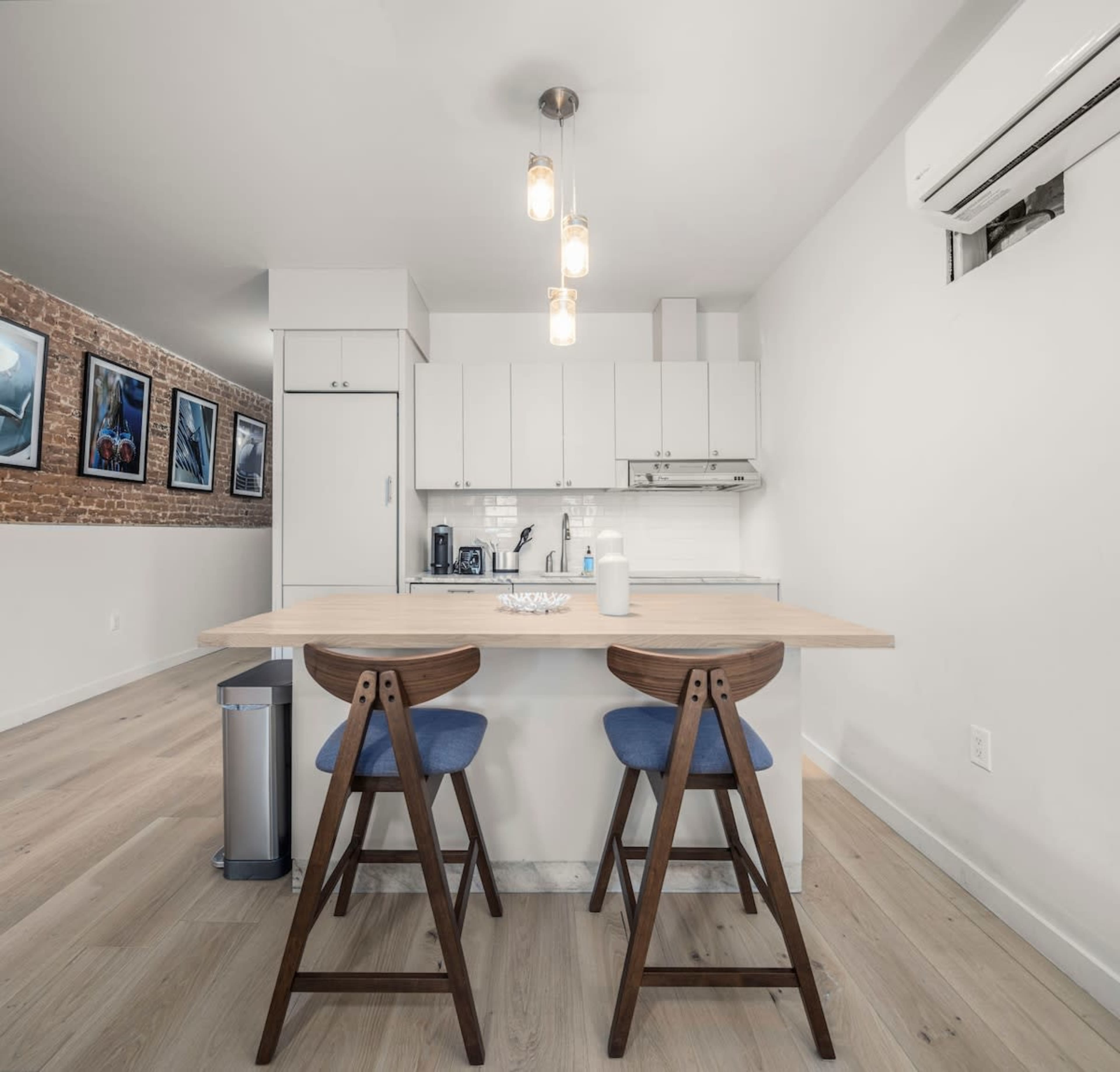 A modern kitchen features a wooden island with two stools and a wall with framed photographs.
