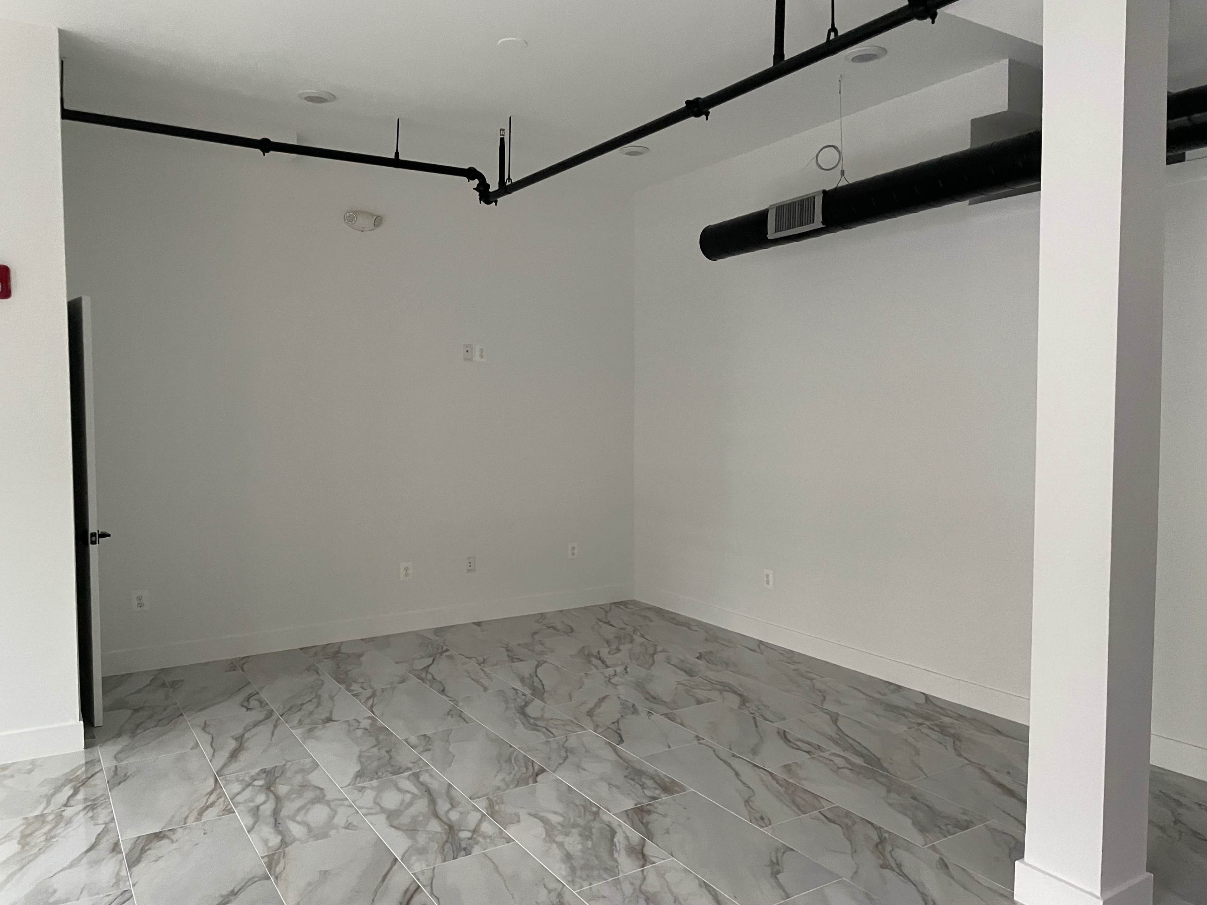 An empty room with light-colored walls and tiled flooring.