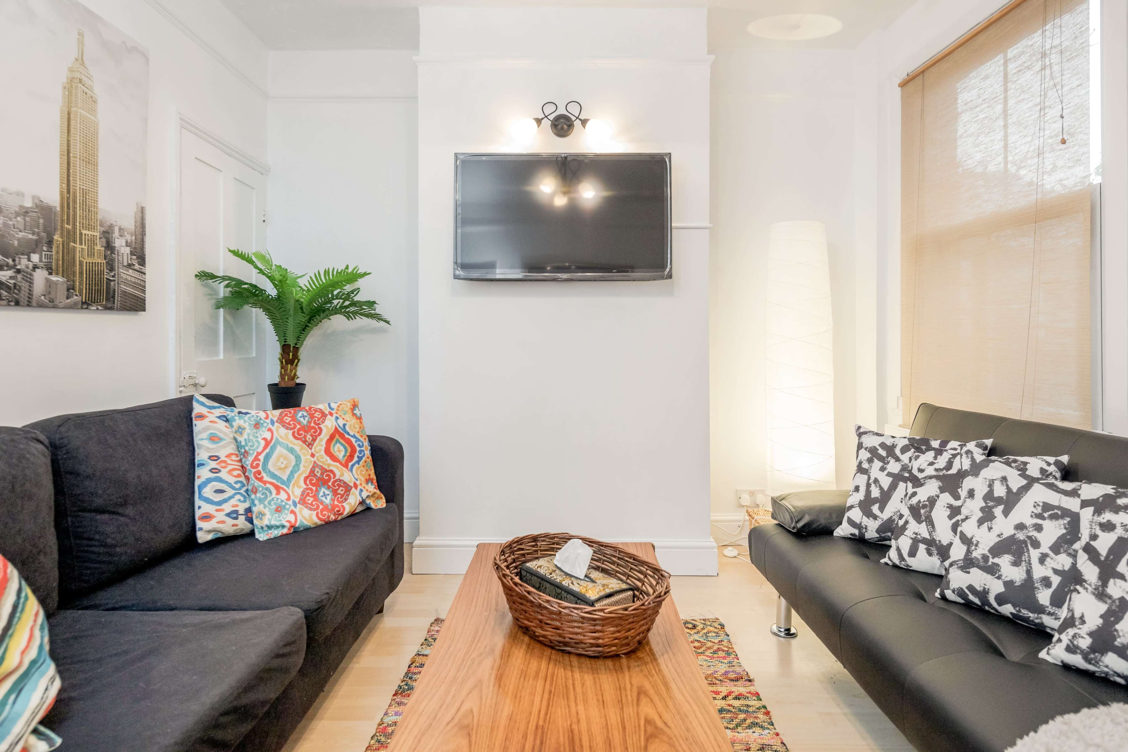 The living room features two sofas, a wooden coffee table, a television mounted on the wall, and a decorative plant.