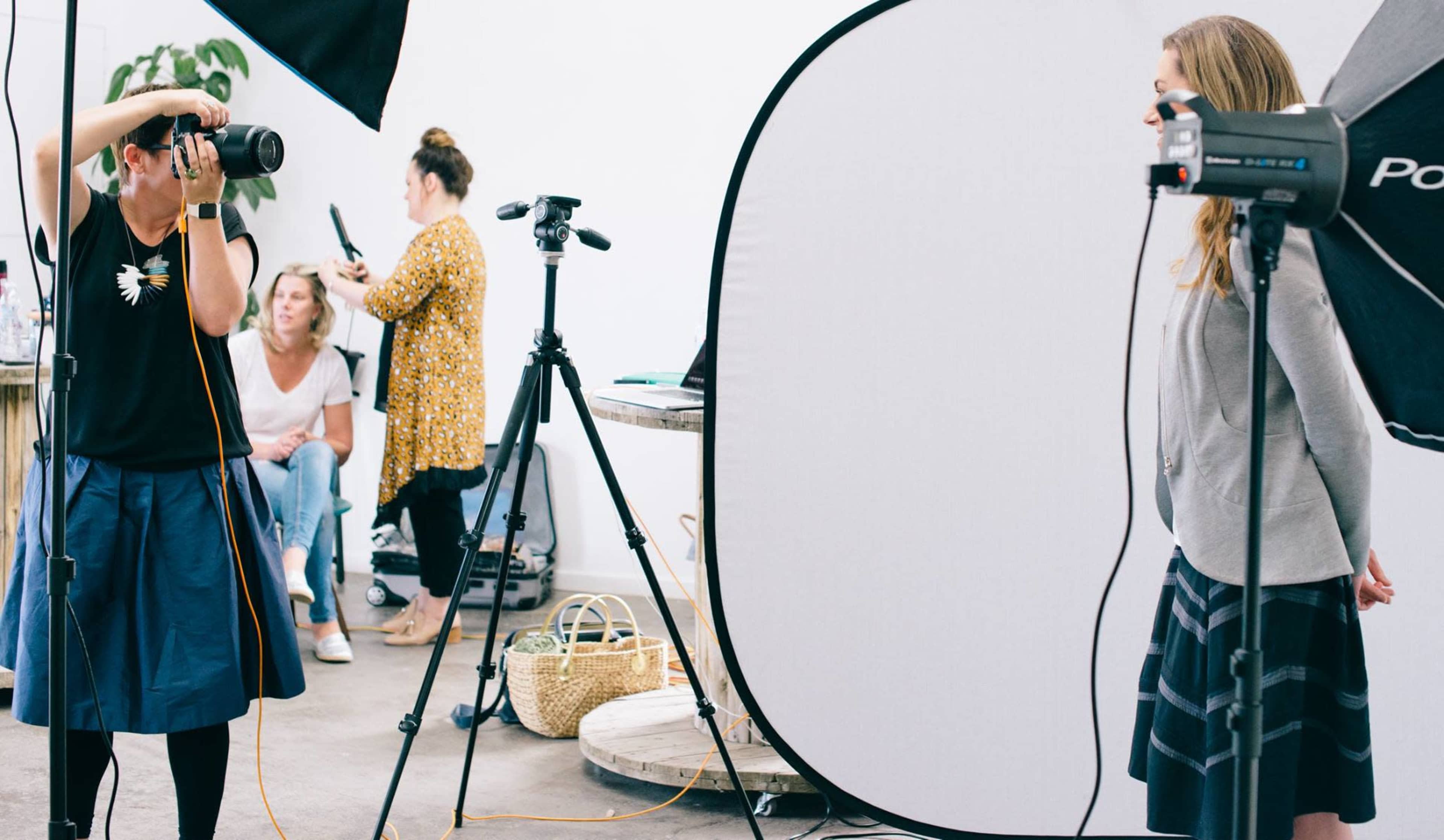 A photographer captures an image of a woman posing in front of a lighting setup, while another person prepares in the background.