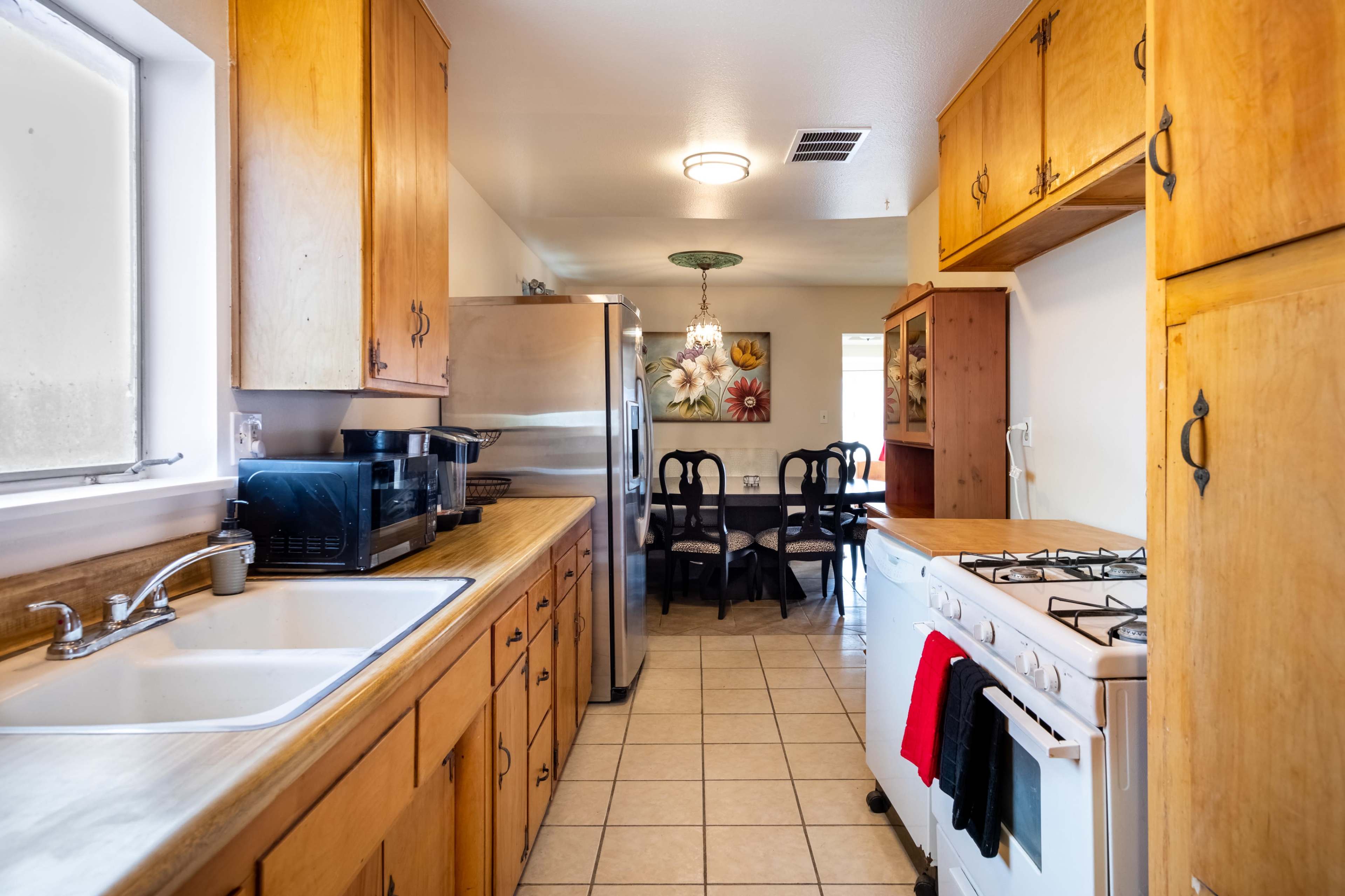 A kitchen features wooden cabinets, a stainless steel refrigerator, and a gas stove, with an adjacent dining area visible in the background.