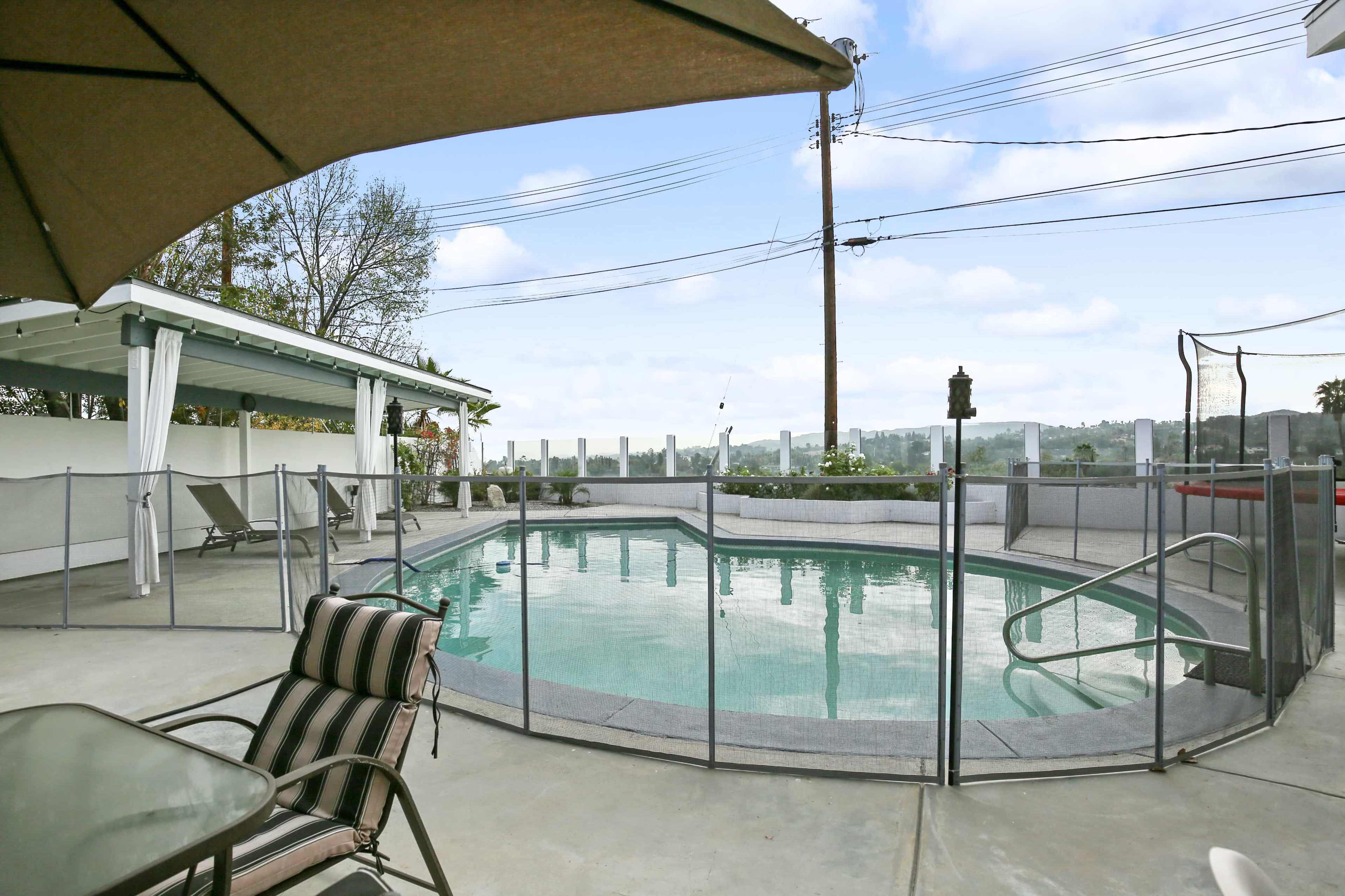 The image shows a fenced swimming pool area with lounge chairs and a view of the surrounding landscape.