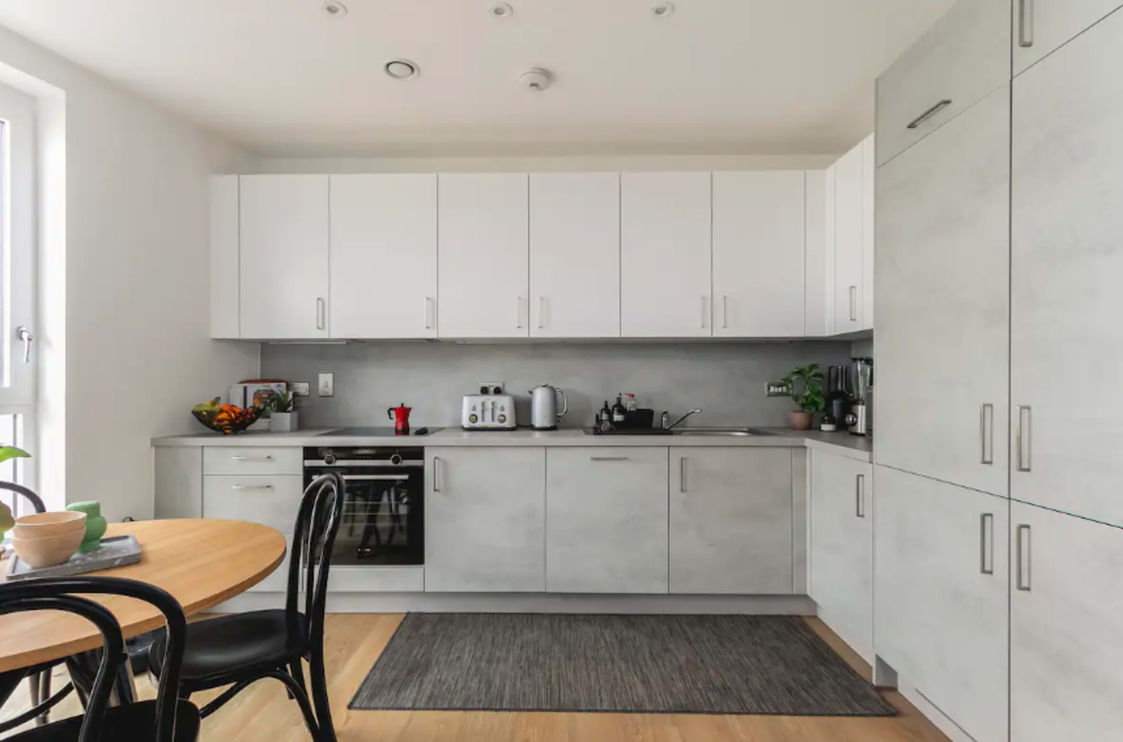 A modern kitchen features light gray cabinetry, a black stove, and a round dining table with black chairs.