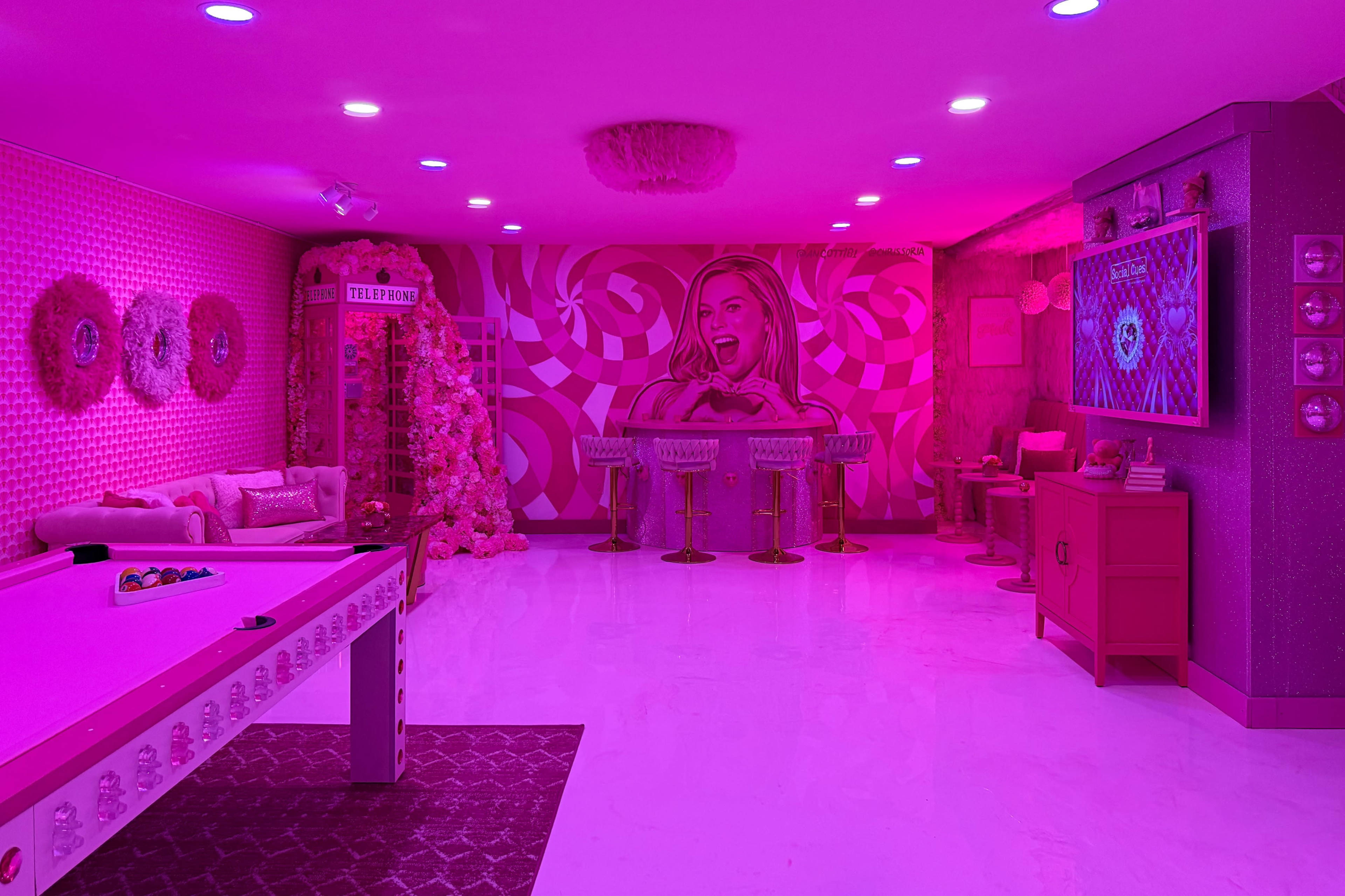 The room features pink walls with a spiral design, a pool table, and bar stools, creating a vibrant and playful atmosphere.