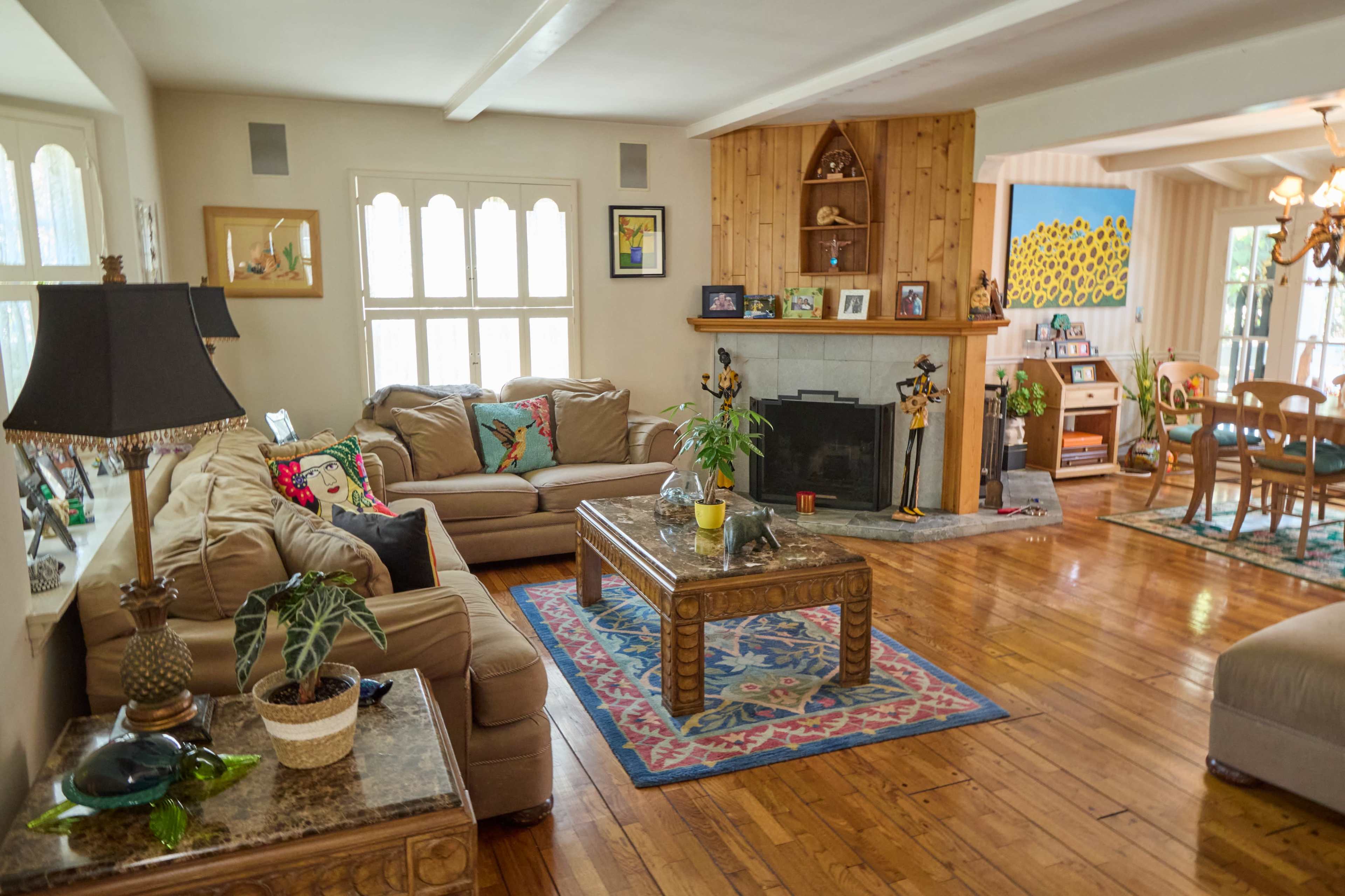 The image depicts a living room with a comfortable seating area, a coffee table, a fireplace, and sunlight illuminating the wooden floors.