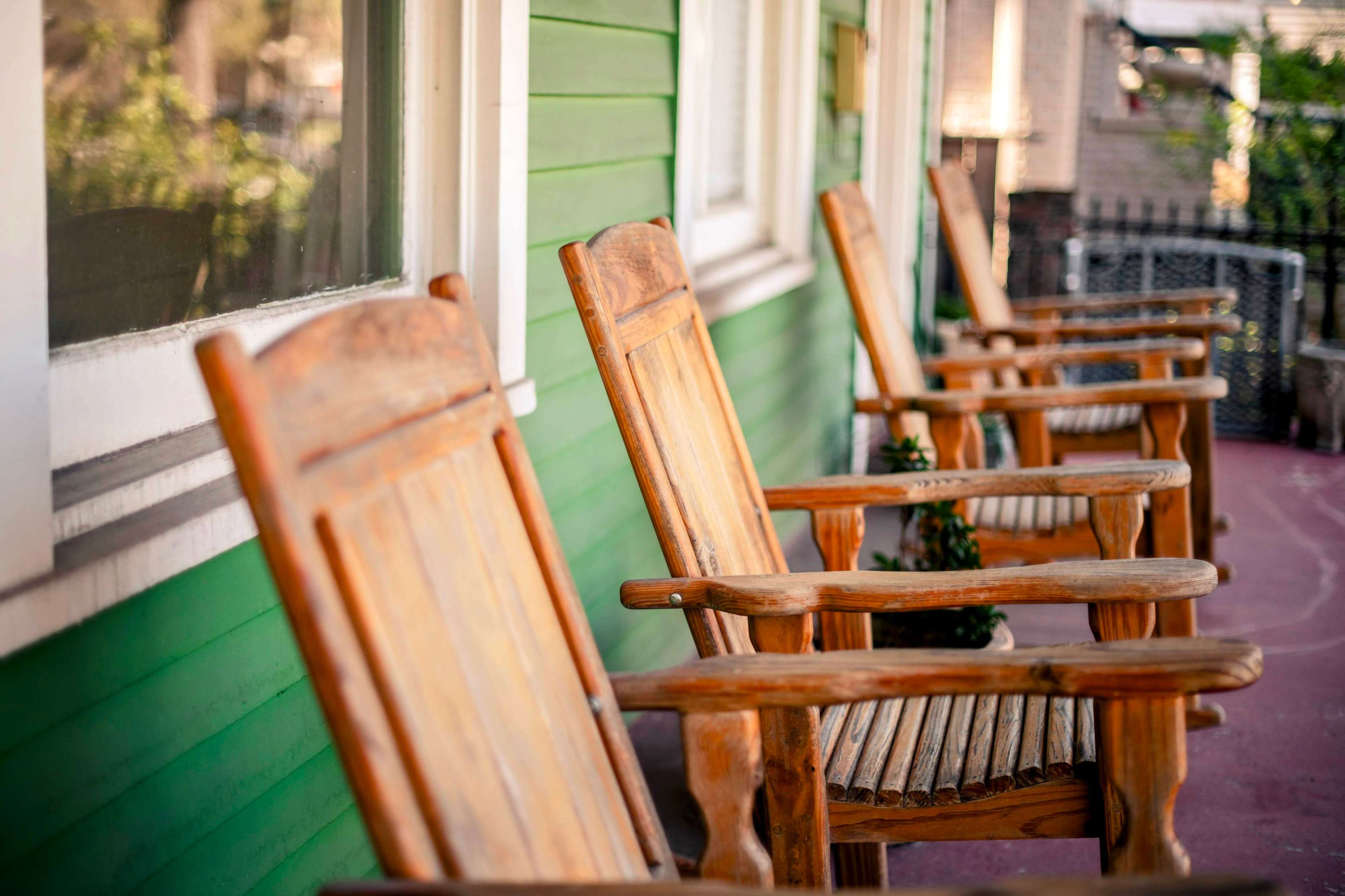 A row of wooden rocking chairs is positioned on a porch with green walls.