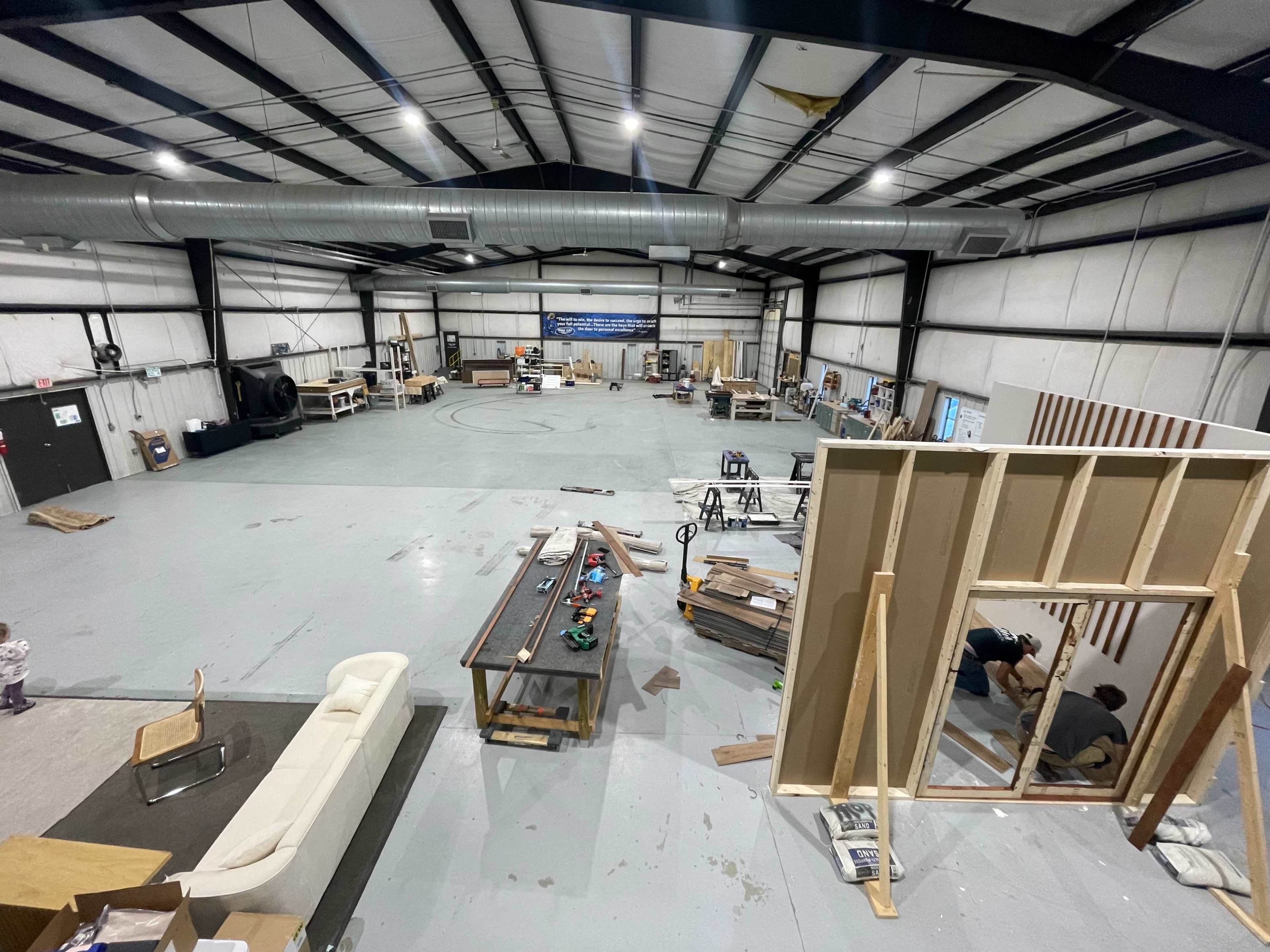 The image shows a large, unfinished industrial space with various construction materials scattered around and a partially built wall in the foreground.