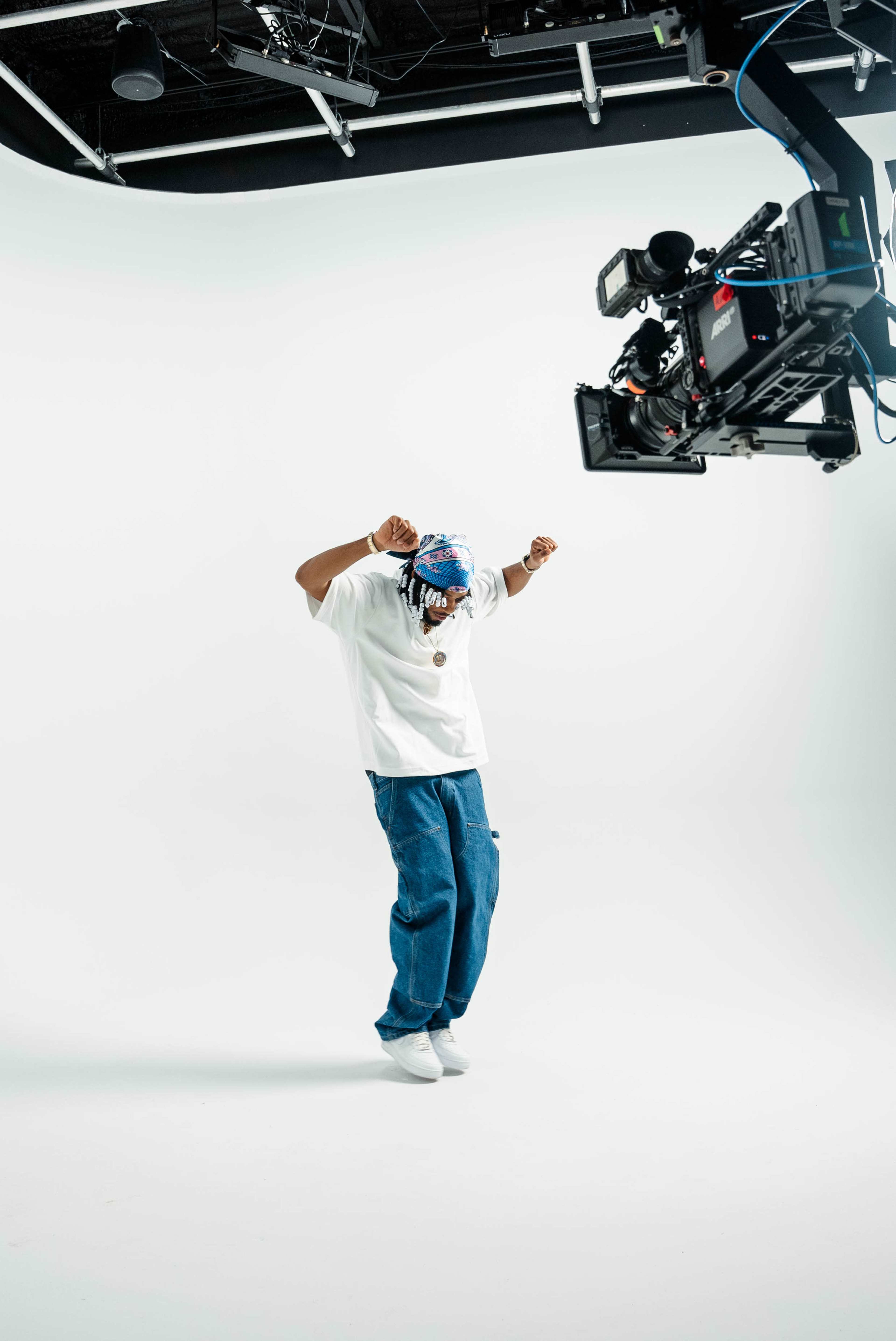 A person wearing a white shirt and blue jeans dances under a camera suspended from a rig.