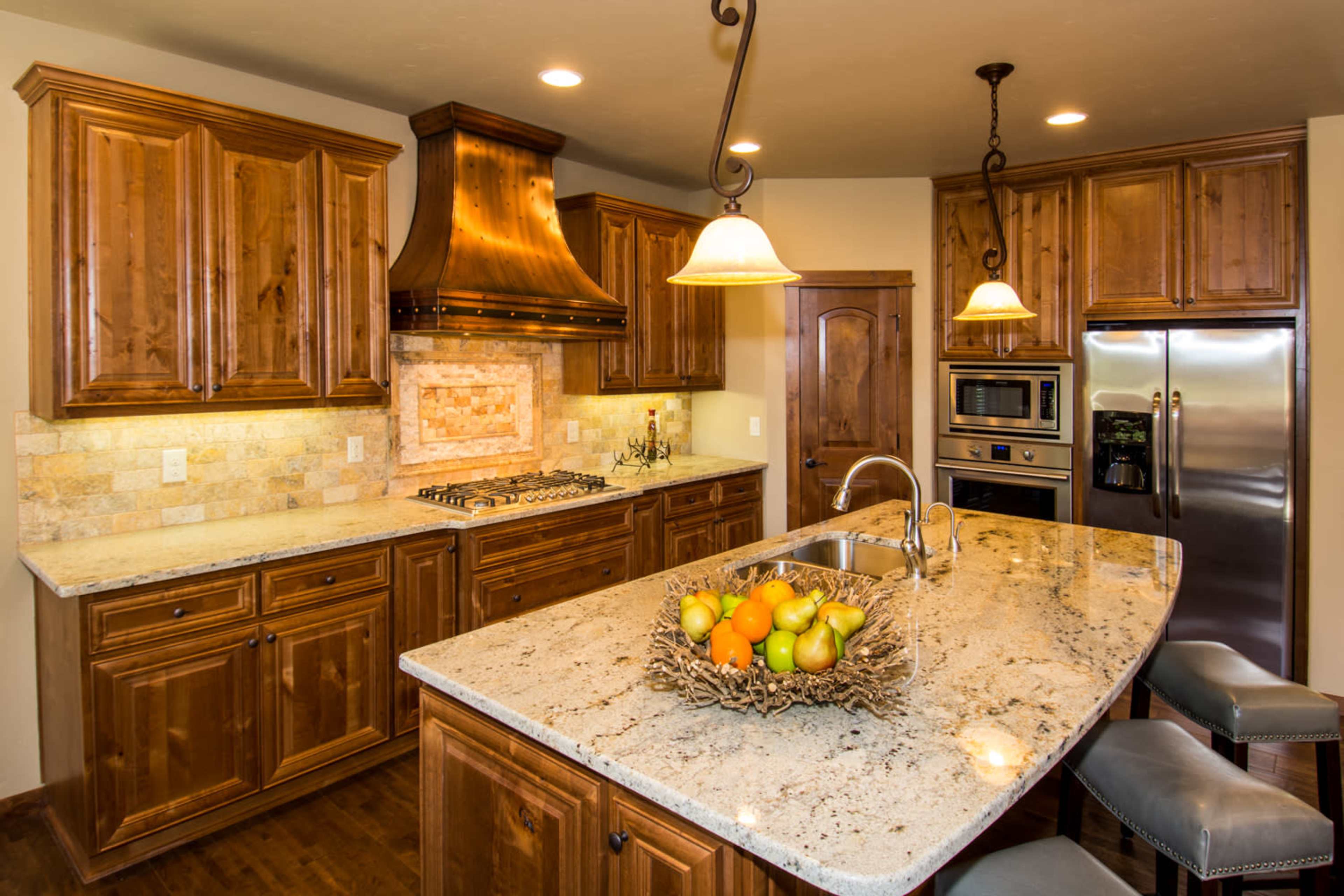 The kitchen features wooden cabinetry, a granite countertop island with a fruit bowl, and stainless steel appliances.