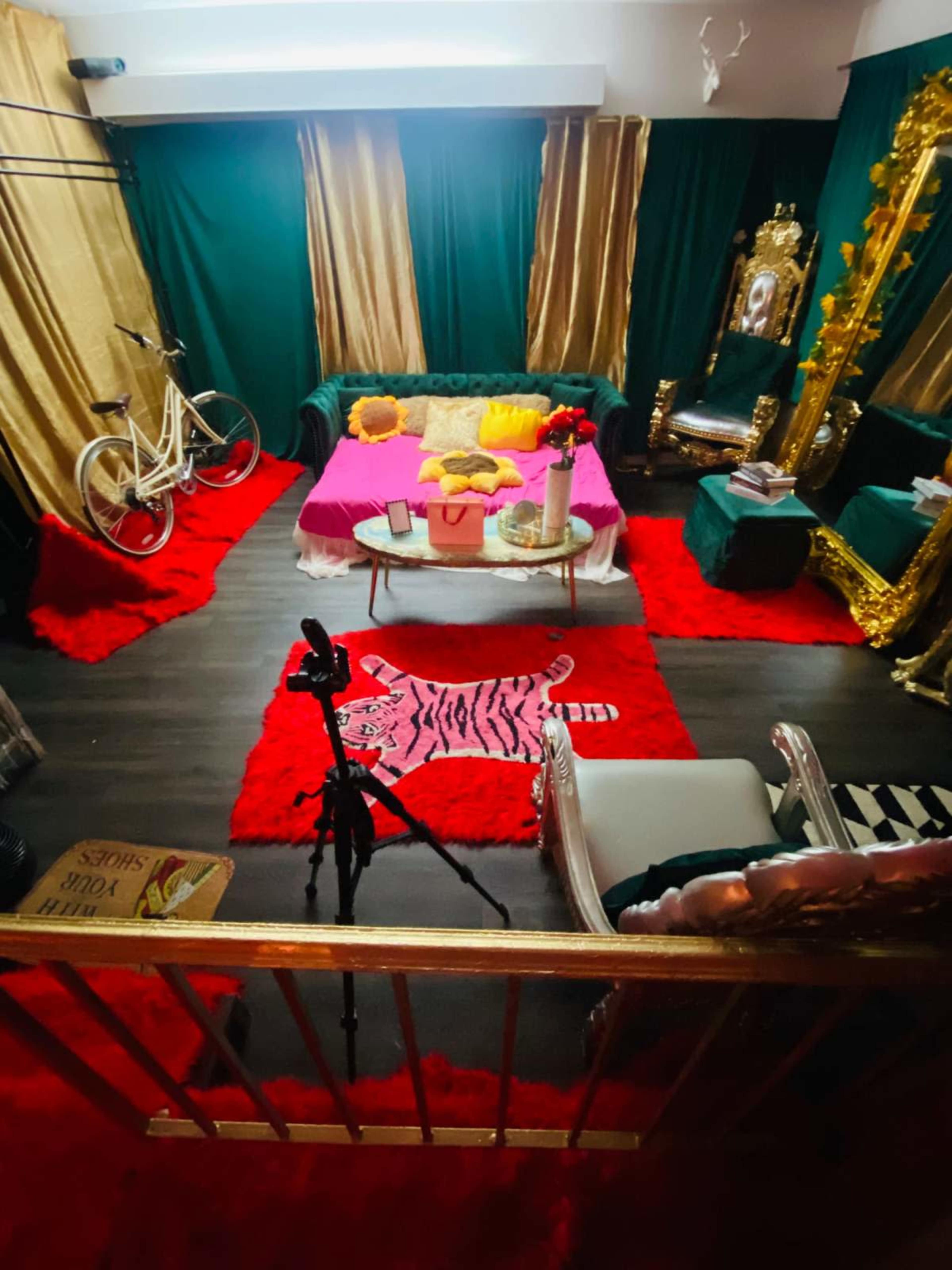 The image shows a colorful room with a gold-accented couch, a bicycle, and a large mirror, all set against green and gold drapery.