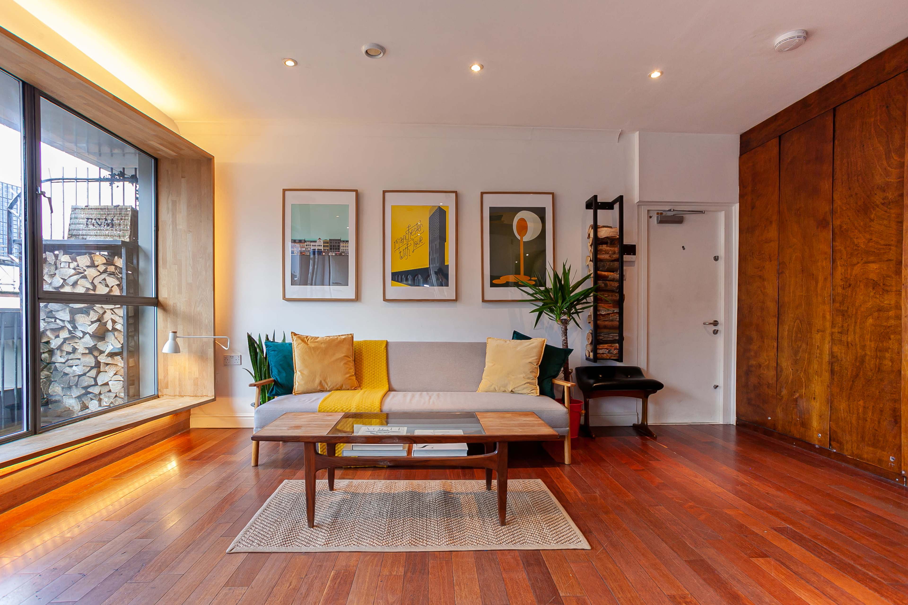 A modern living room with a sofa, a coffee table, and framed artwork on the walls, featuring a large window that allows natural light to enter the space.