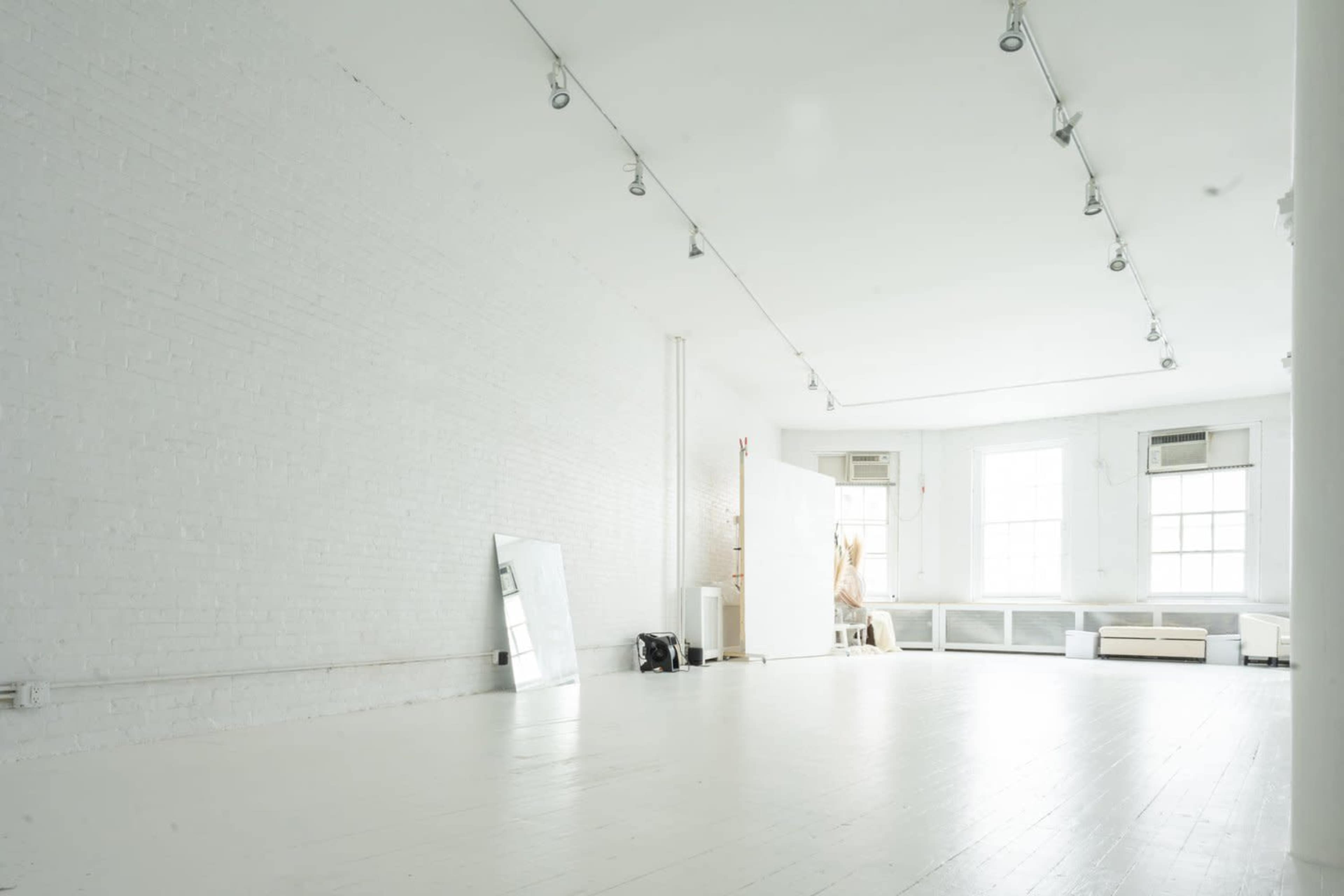 A spacious, empty studio with white brick walls, hardwood floors, and large windows.