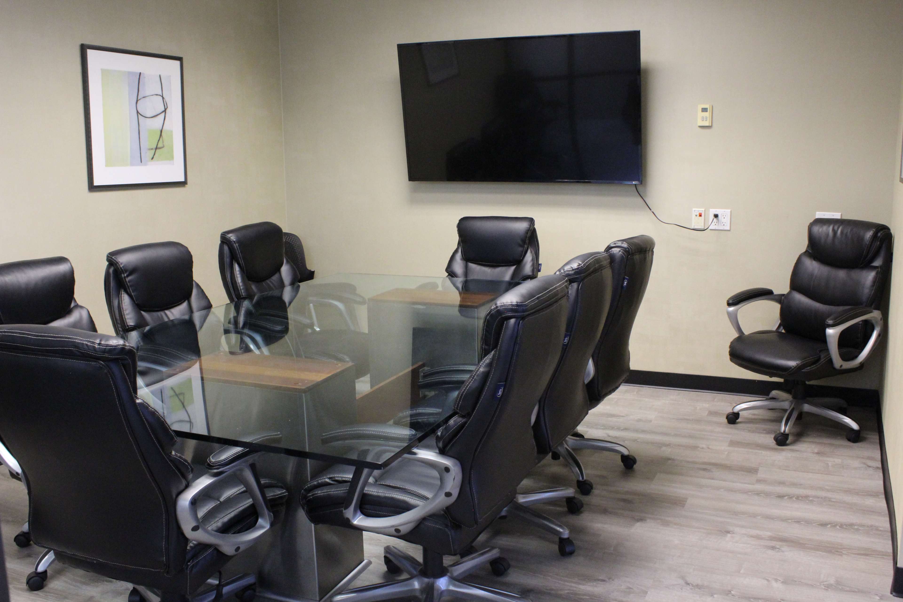 A conference room features a glass table surrounded by black leather chairs and a wall-mounted television.