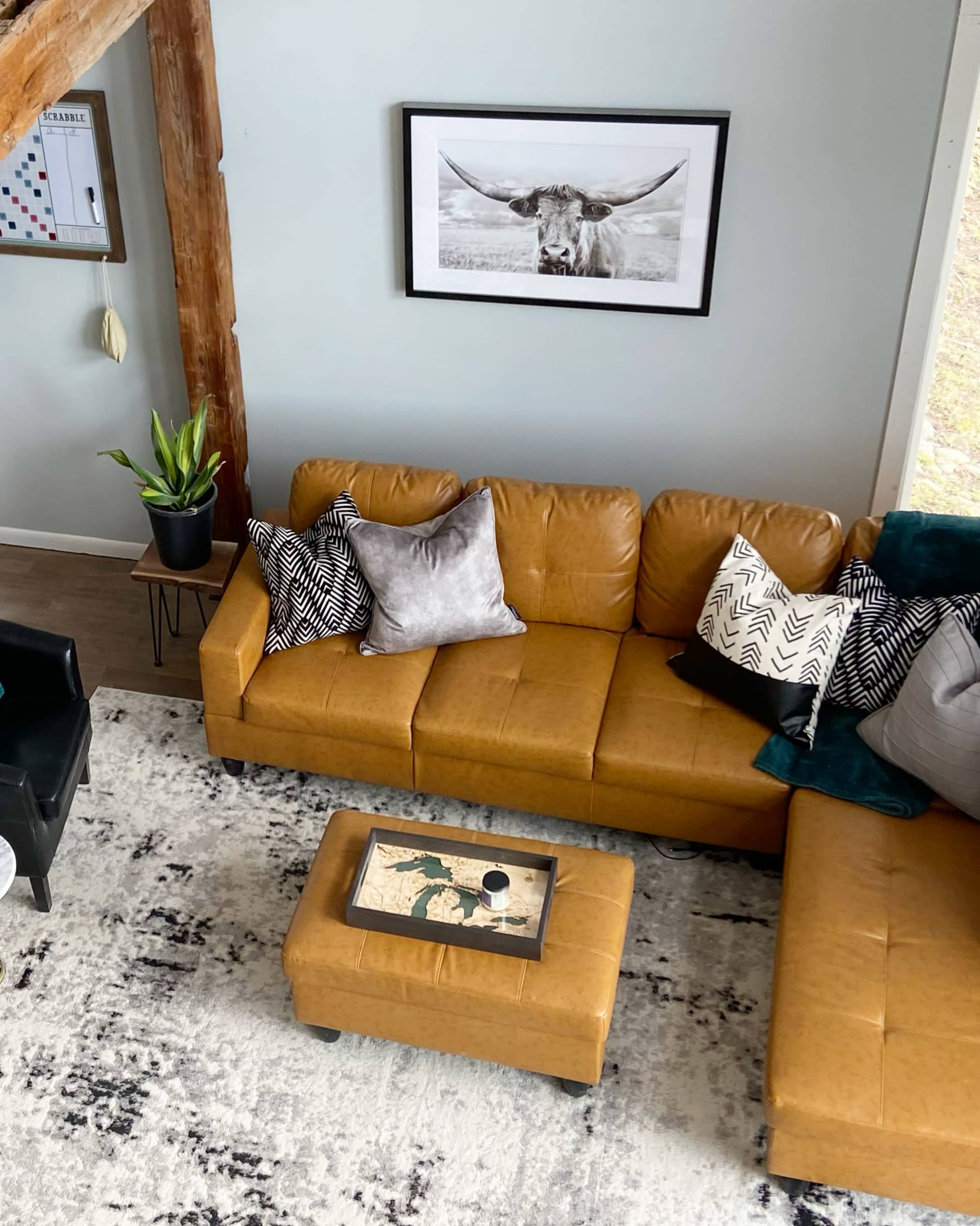 A brown leather sectional sofa with decorative pillows is arranged around a coffee table on a patterned rug in a living room.