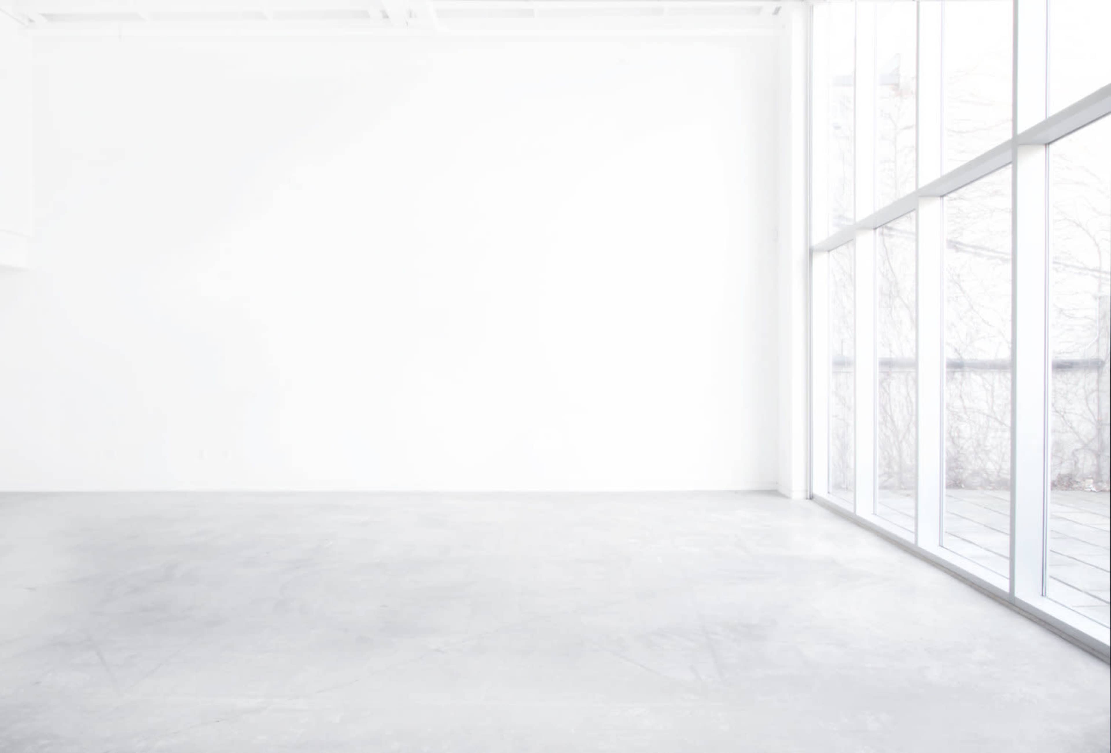 A minimalistic, empty room with a gray concrete floor and large windows letting in natural light.
