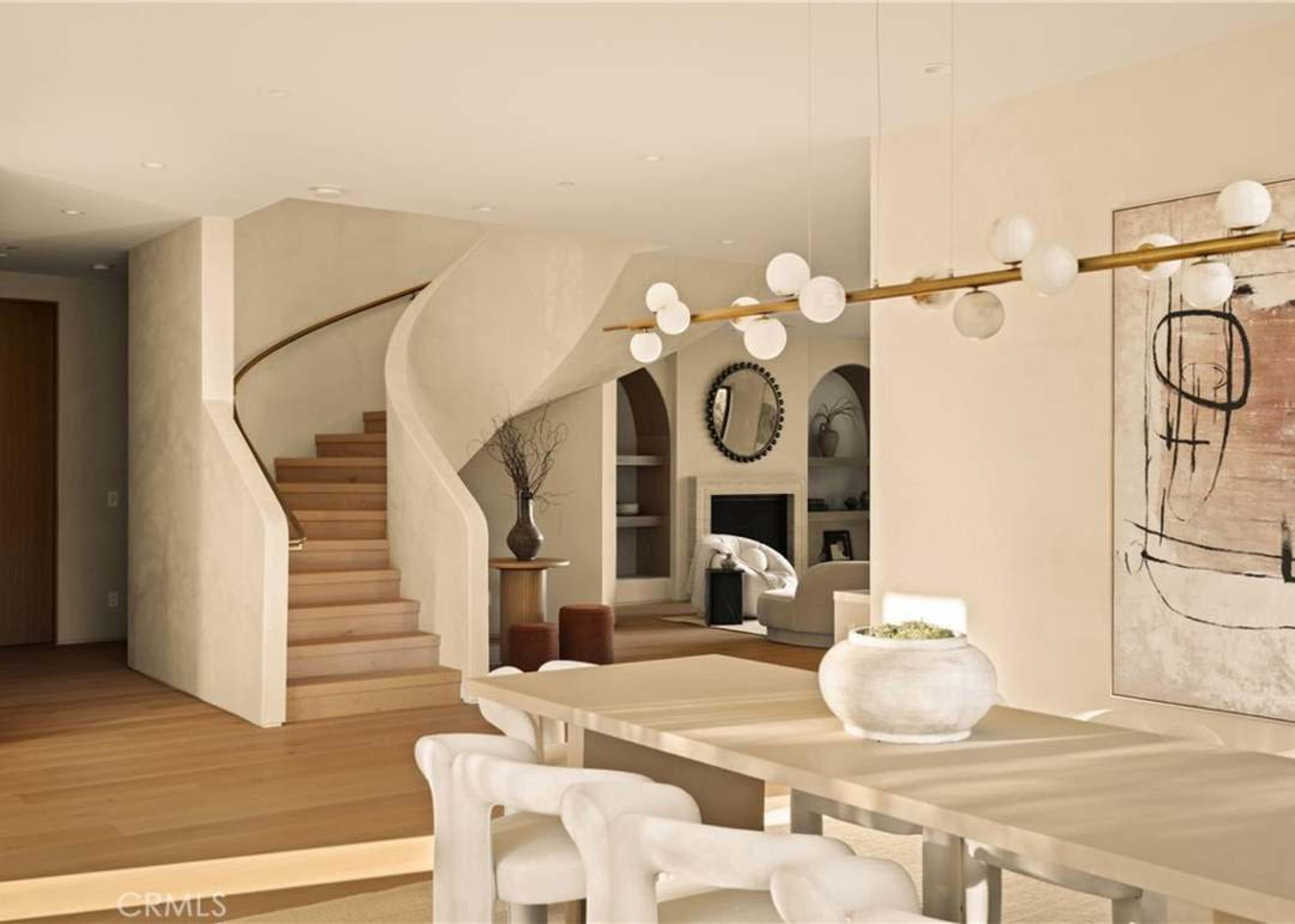 The image shows a modern open-concept living space featuring a dining area with a rectangular table, a staircase in the background, and a stylishly arranged sitting area with a fireplace.