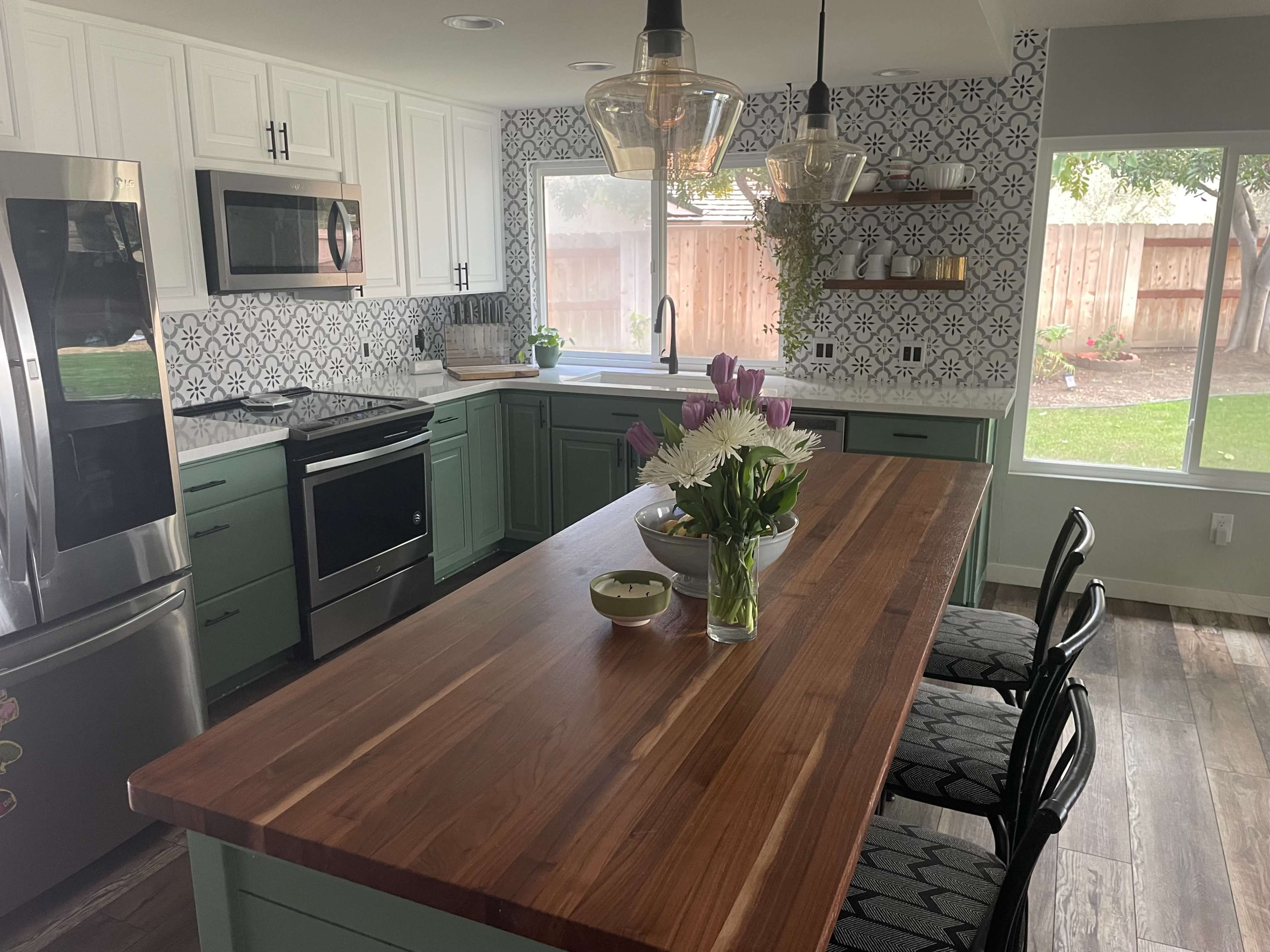 A modern kitchen featuring a large wooden island, stainless steel appliances, and a decorative backsplash with patterned tiles.