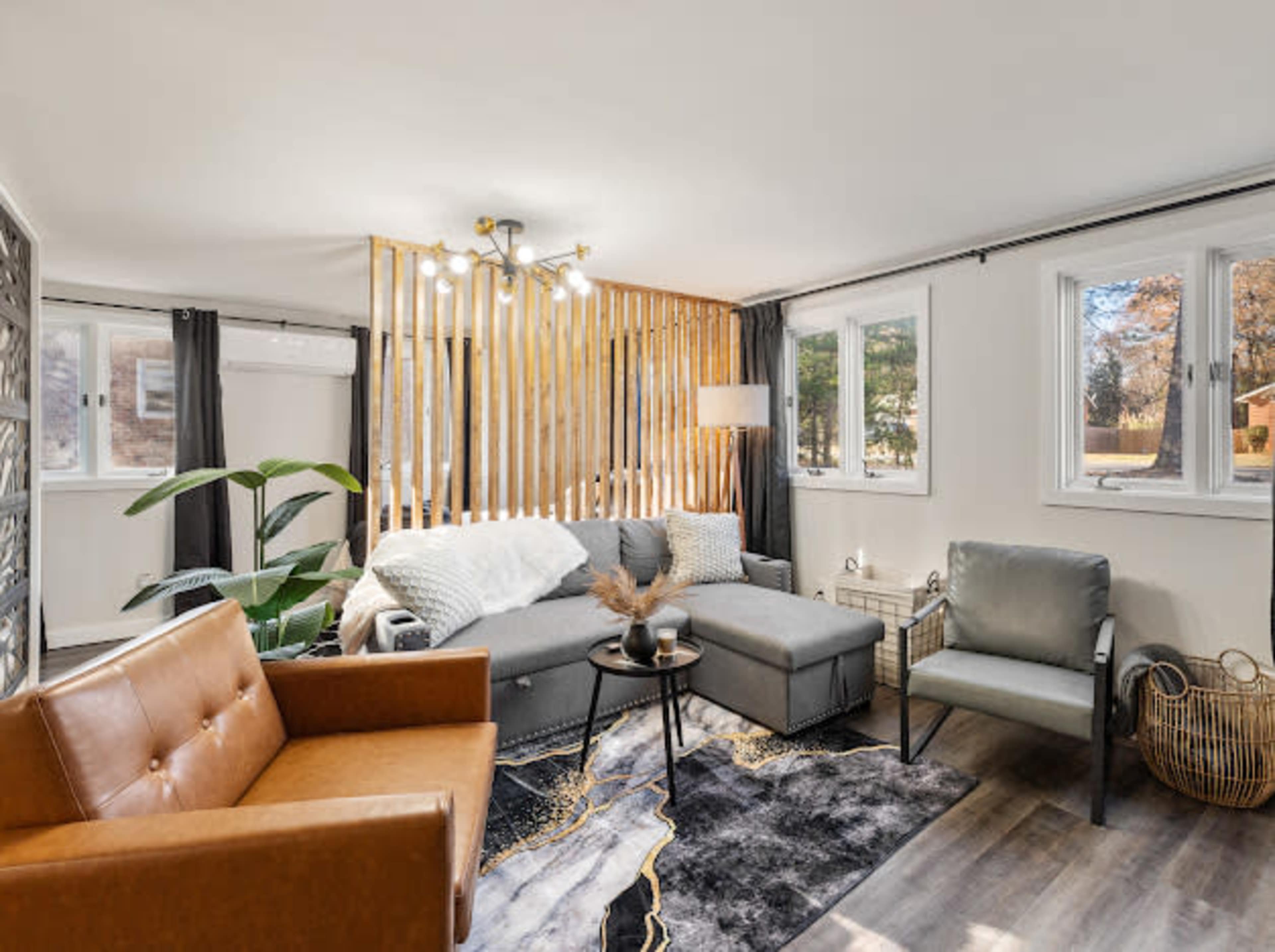 A modern living room featuring a sectional sofa, a brown leather chair, light wood paneling, and large windows providing natural light.