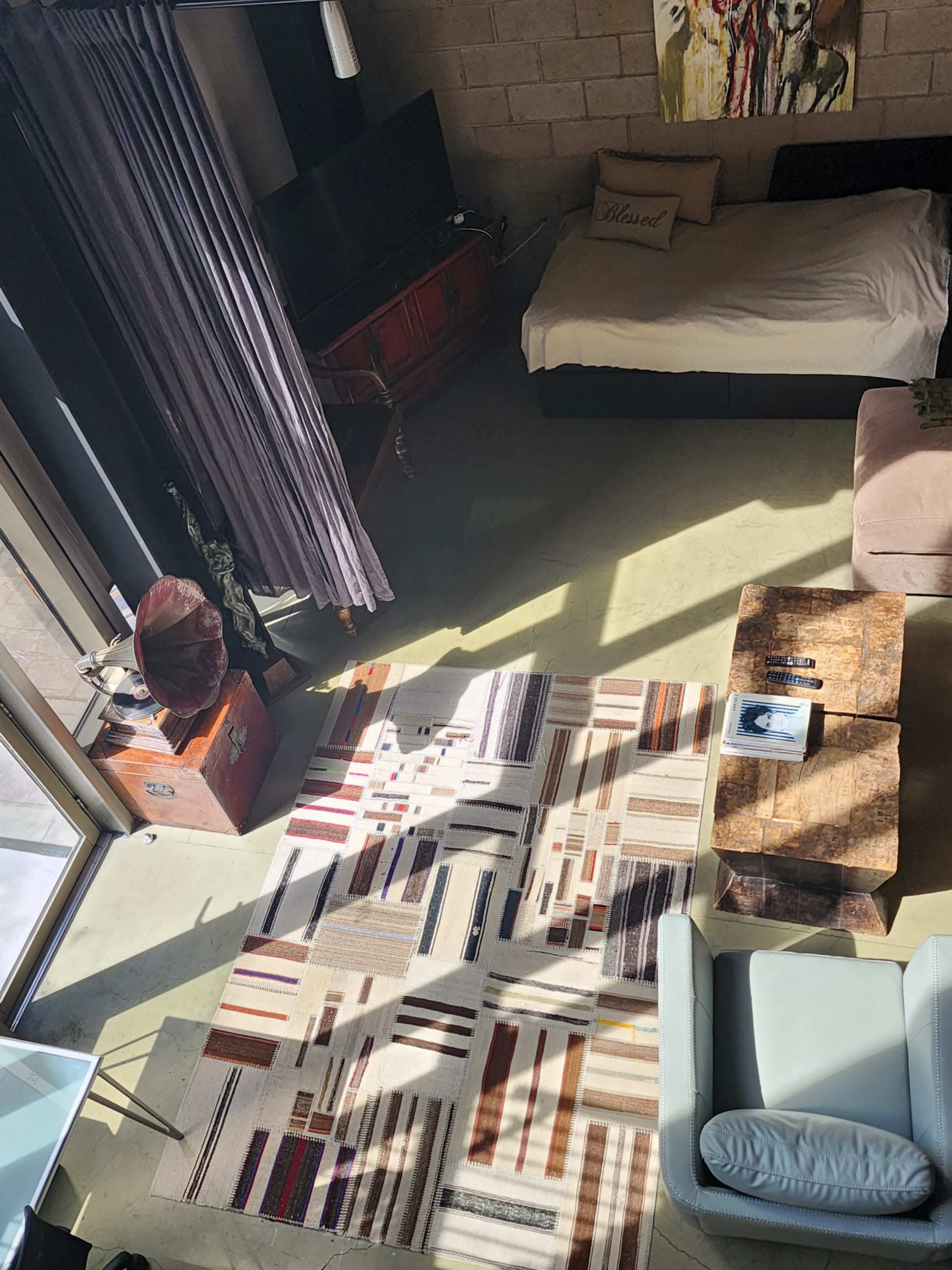 A modern living space with a bed, a couch, a rug featuring geometric patterns, and large windows allowing natural light to enter.