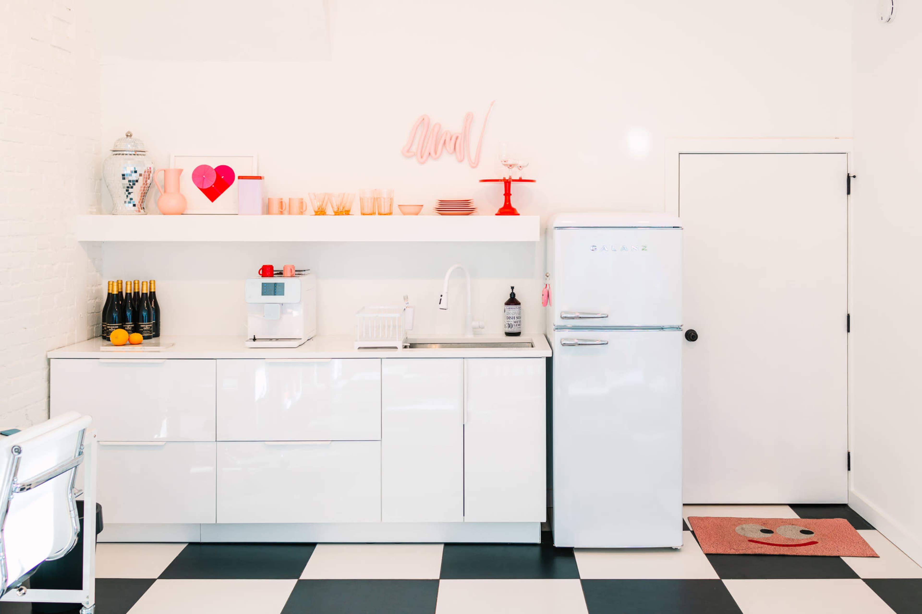 A modern kitchen features white cabinetry, a vintage-style refrigerator, and a black and white checkered floor.