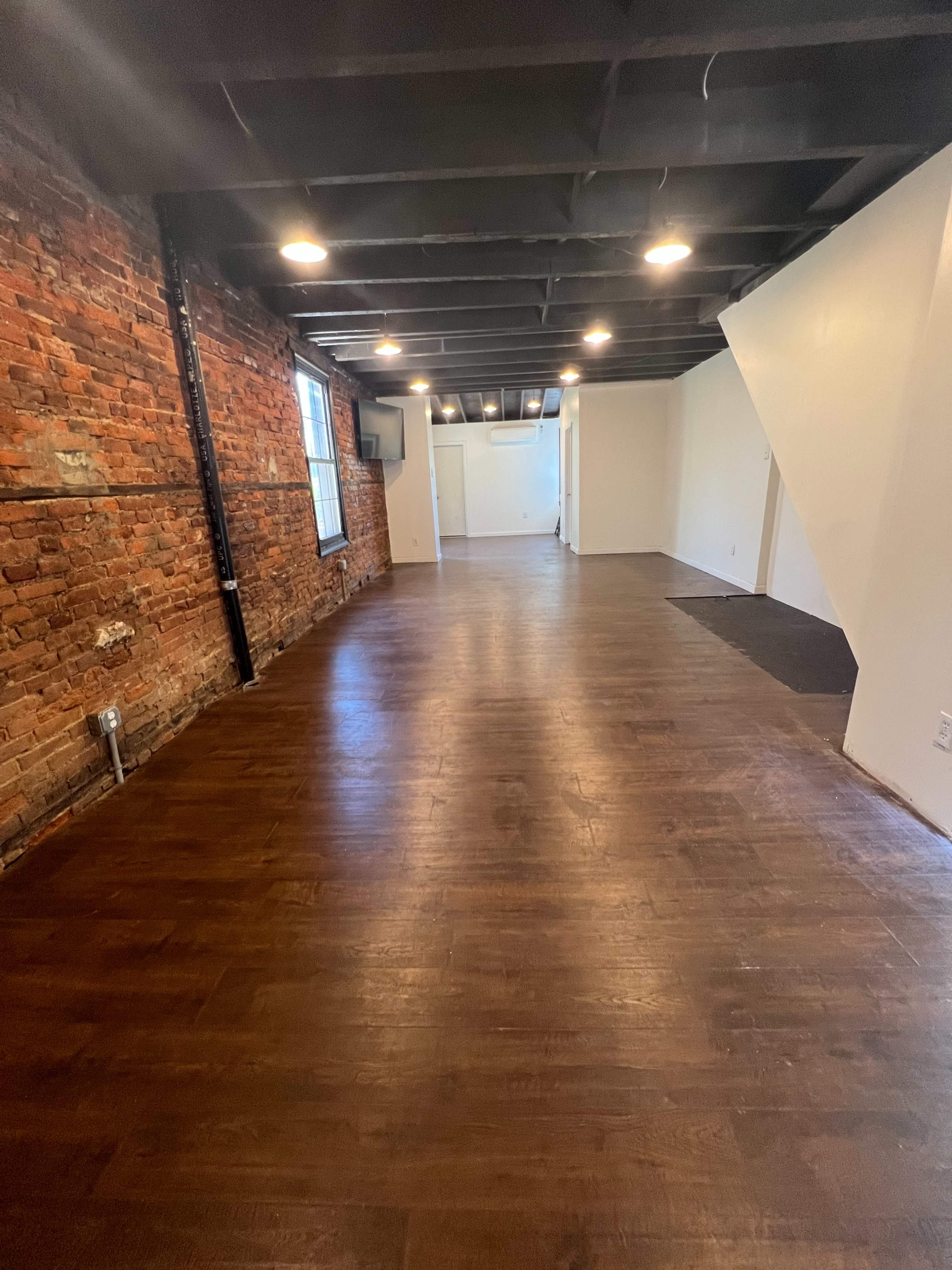 A spacious, empty interior room featuring exposed brick walls and hardwood flooring.