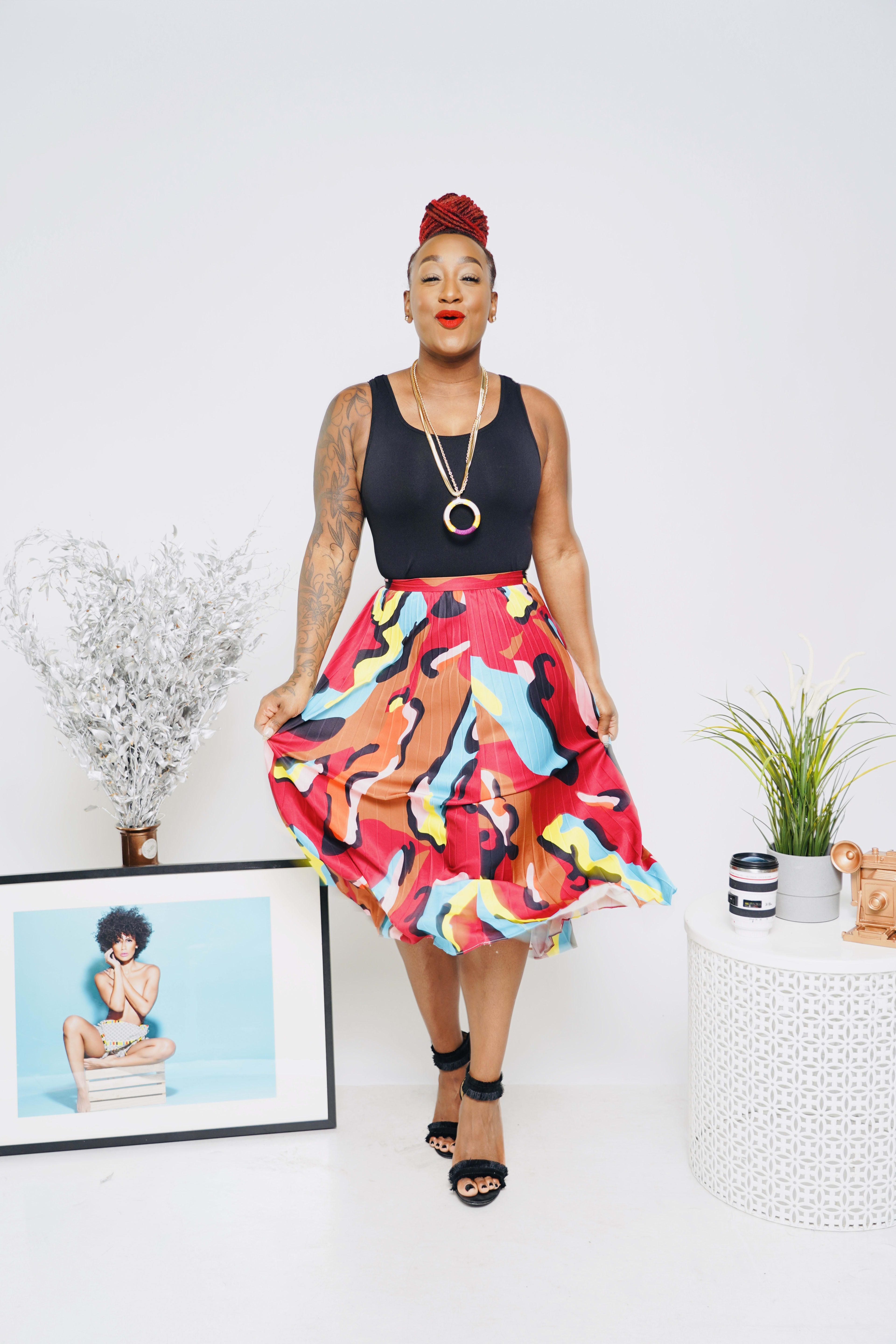 A woman with a colourful dress posing next to a picture frame and plants during a fashion photo shoot.