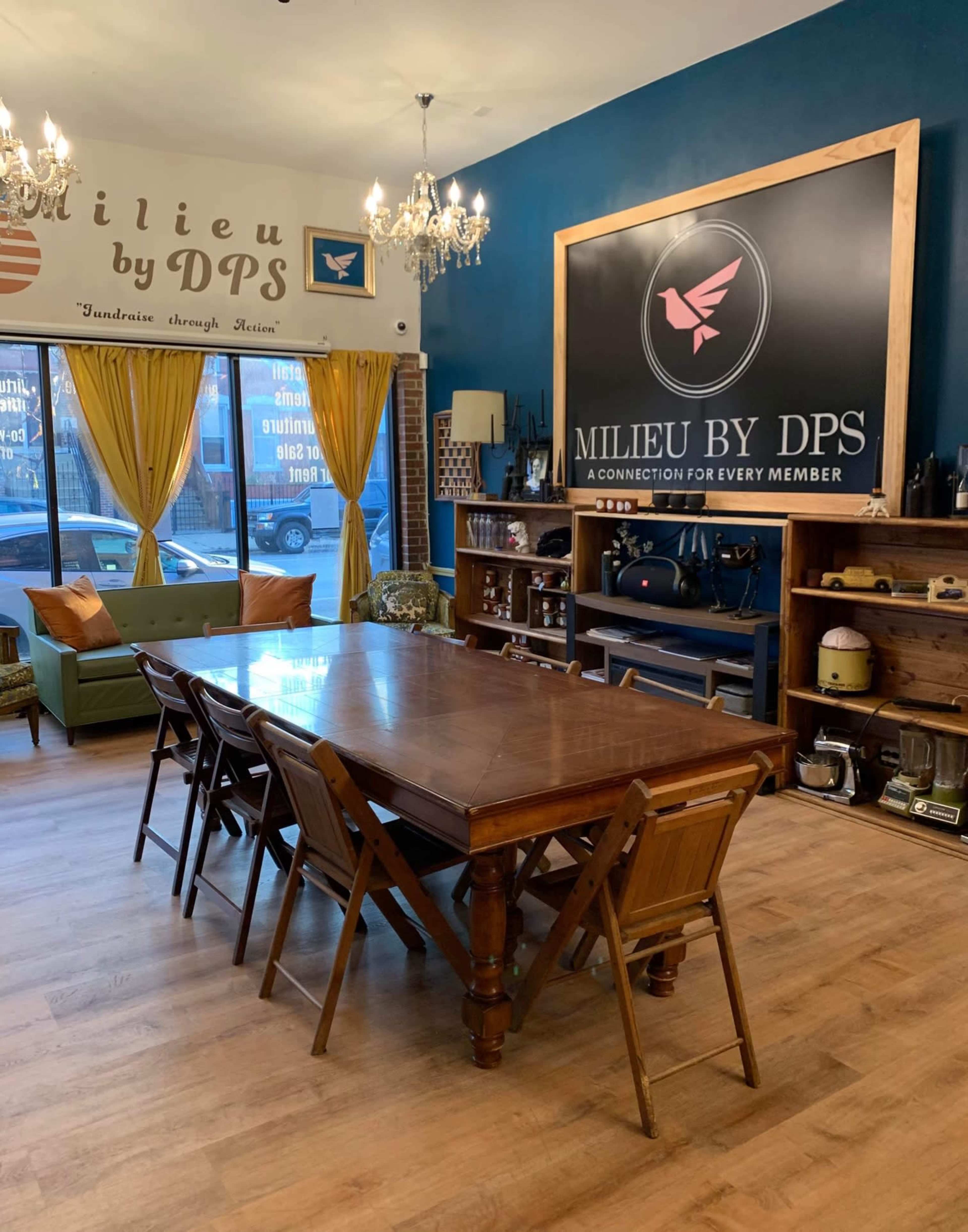 A spacious room with a long wooden table surrounded by folding chairs, a logo display on the wall, and large windows adorned with yellow curtains.