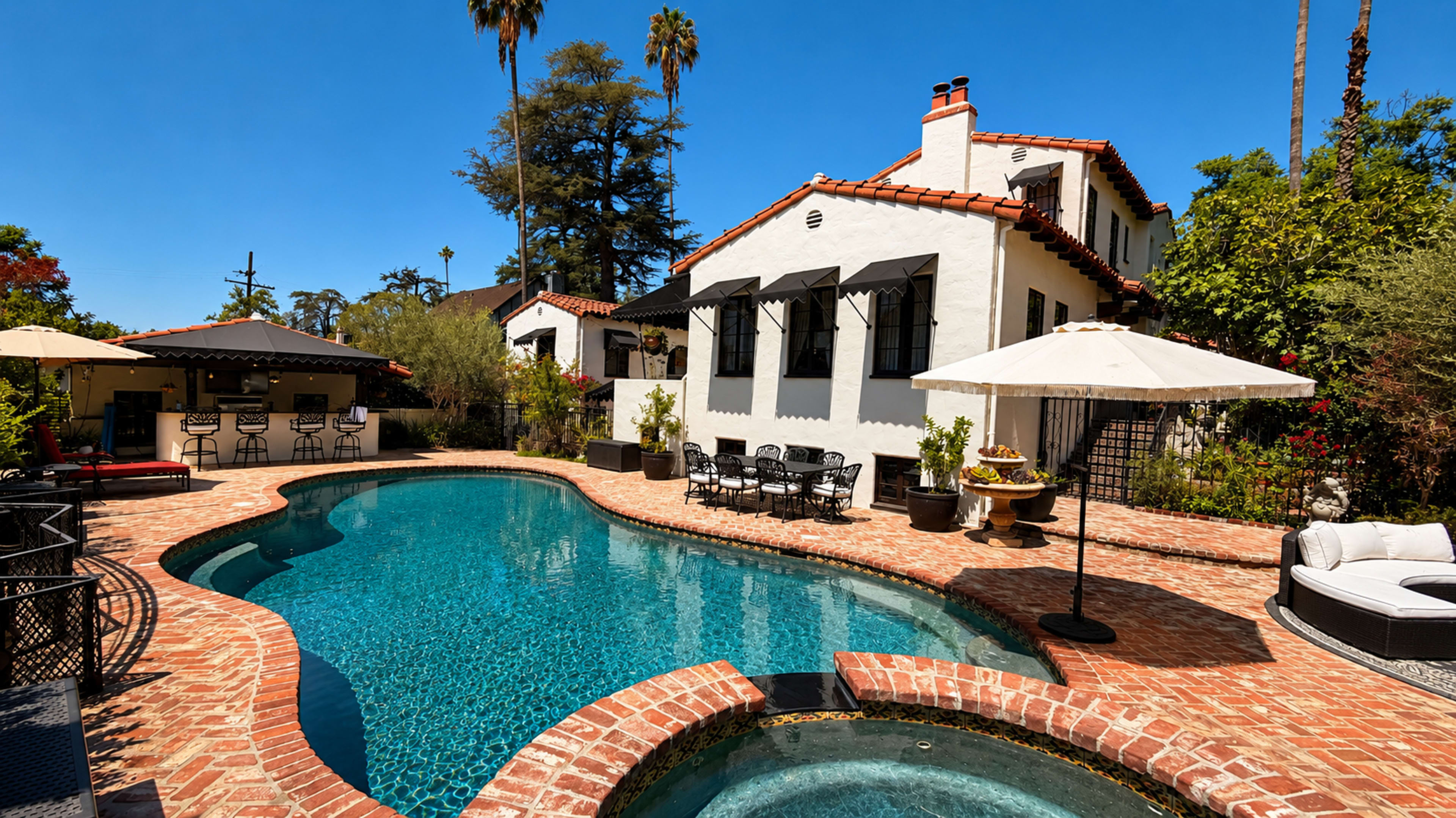 The image shows a landscaped backyard with a swimming pool, surrounded by brick paving and equipped with loungers and umbrellas, adjacent to a two-story house with a tiled roof.