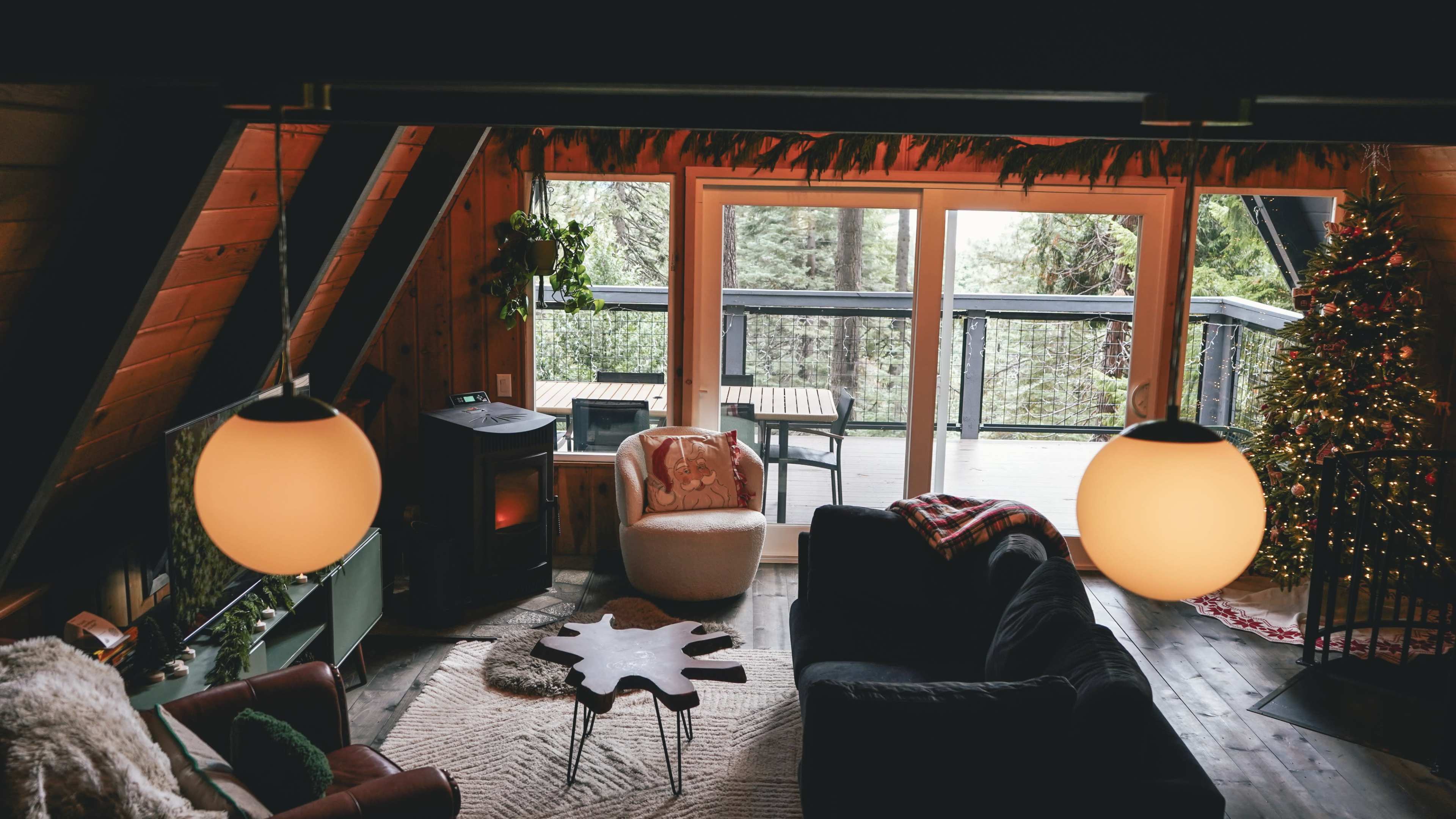 A cozy living room features a comfortable seating area, a coffee table with a unique shape, and large windows that open to a deck surrounded by trees.