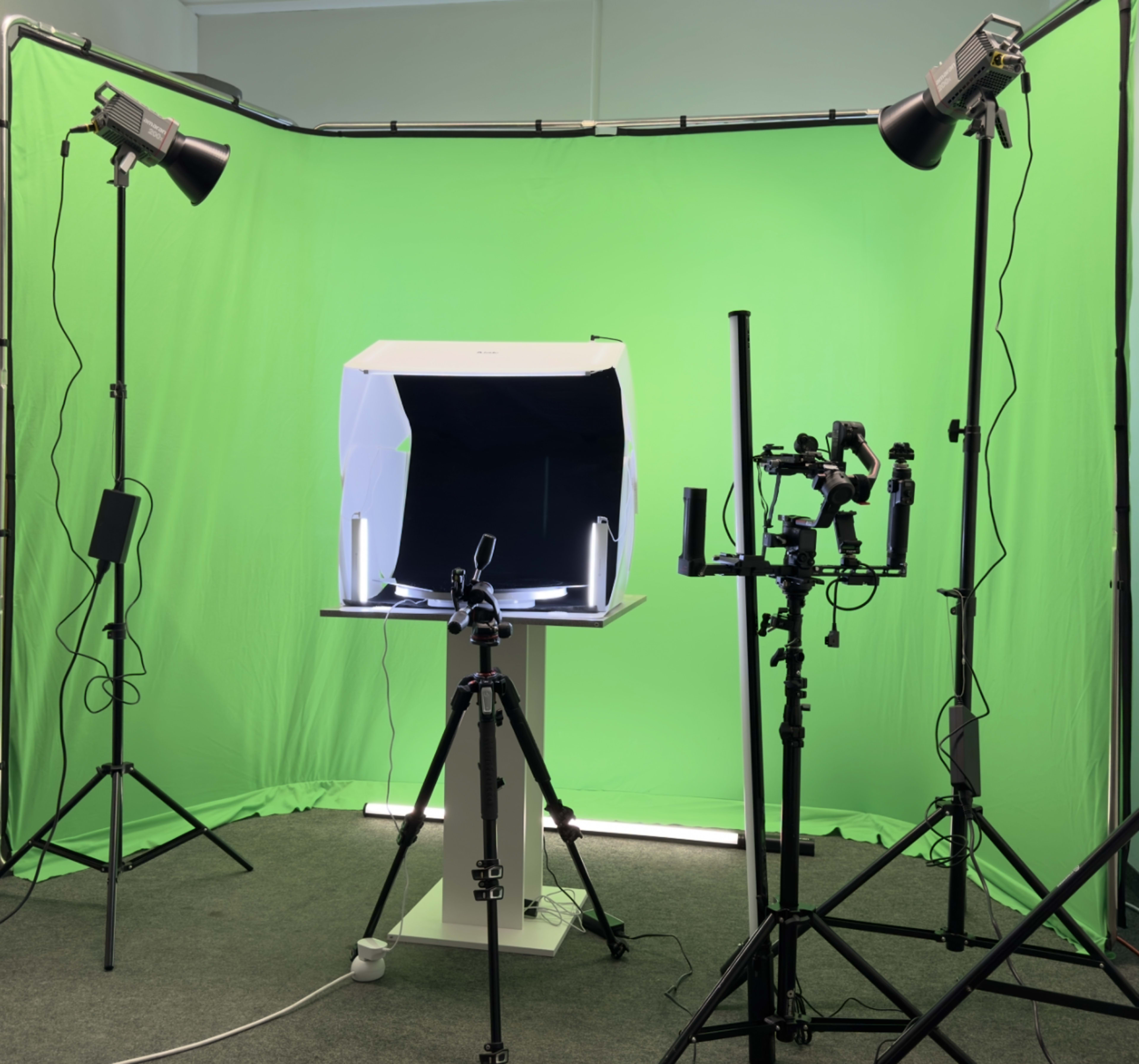 The image shows a photography setup featuring a lightbox on a table, surrounded by three tripods, photography lights, and a green backdrop.