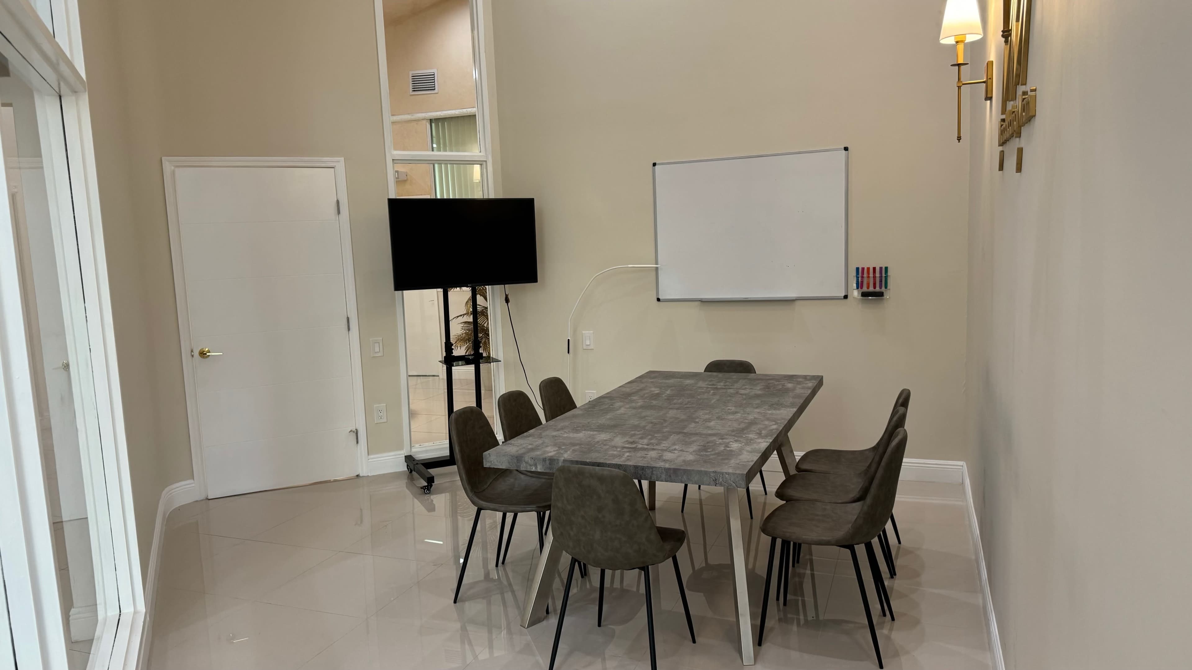 The image shows a modern conference room featuring a rectangular table surrounded by six chairs, a whiteboard on the wall, and a television on a stand.