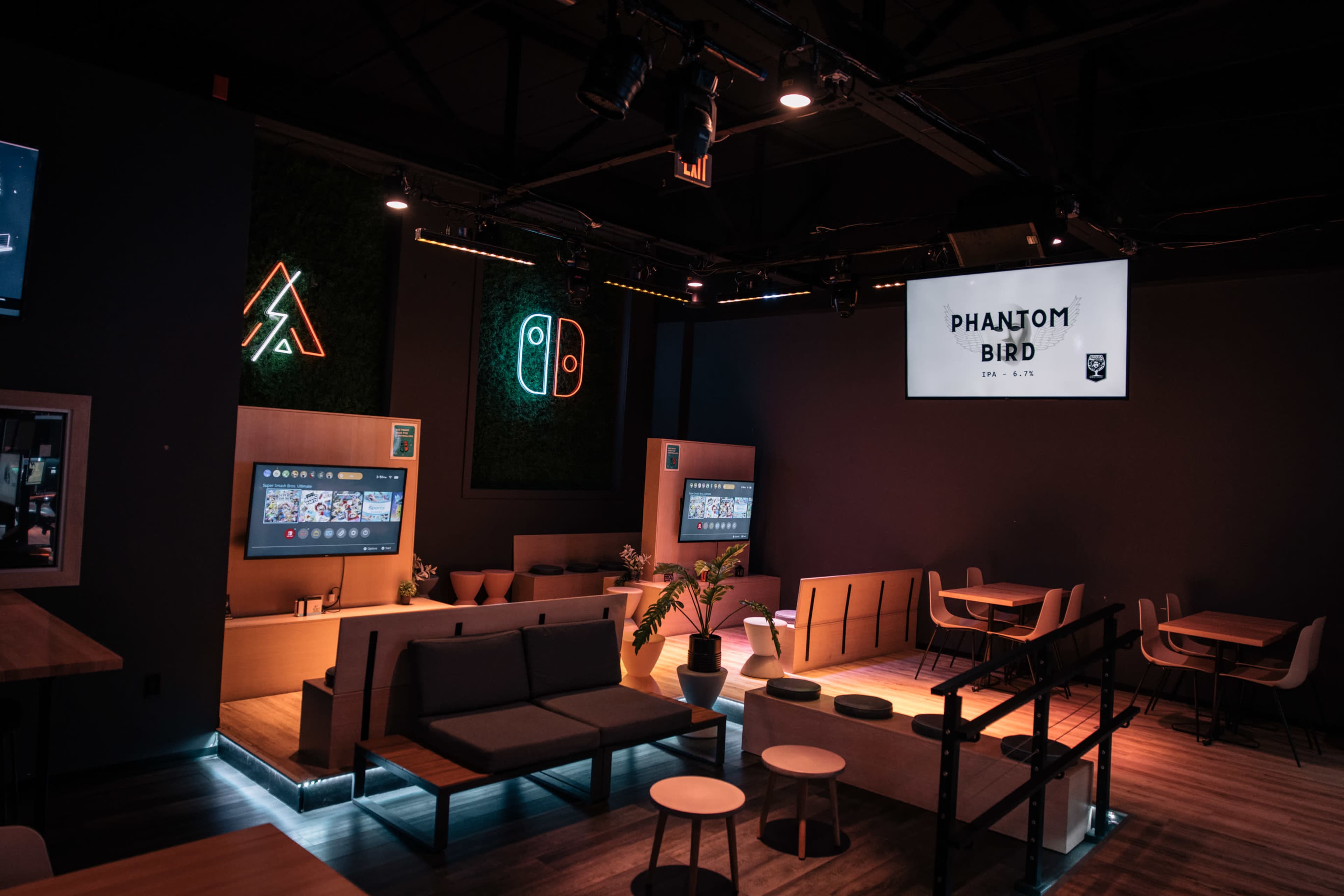 A modern lounge area with seating arrangements, digital screens on the walls, and neon signage.