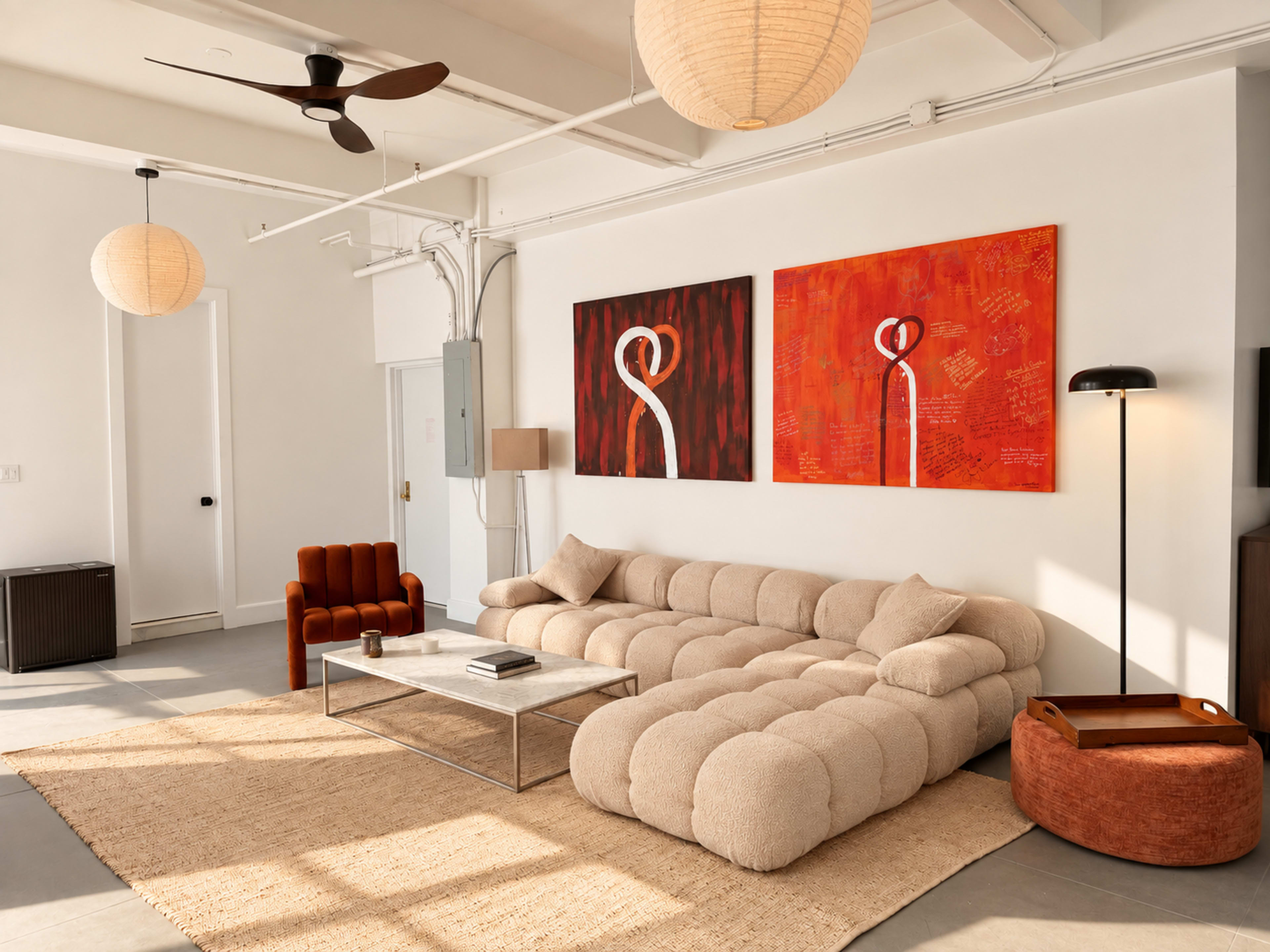 The image shows a modern living room featuring a plush sectional sofa, two abstract paintings, a coffee table, and various light fixtures.