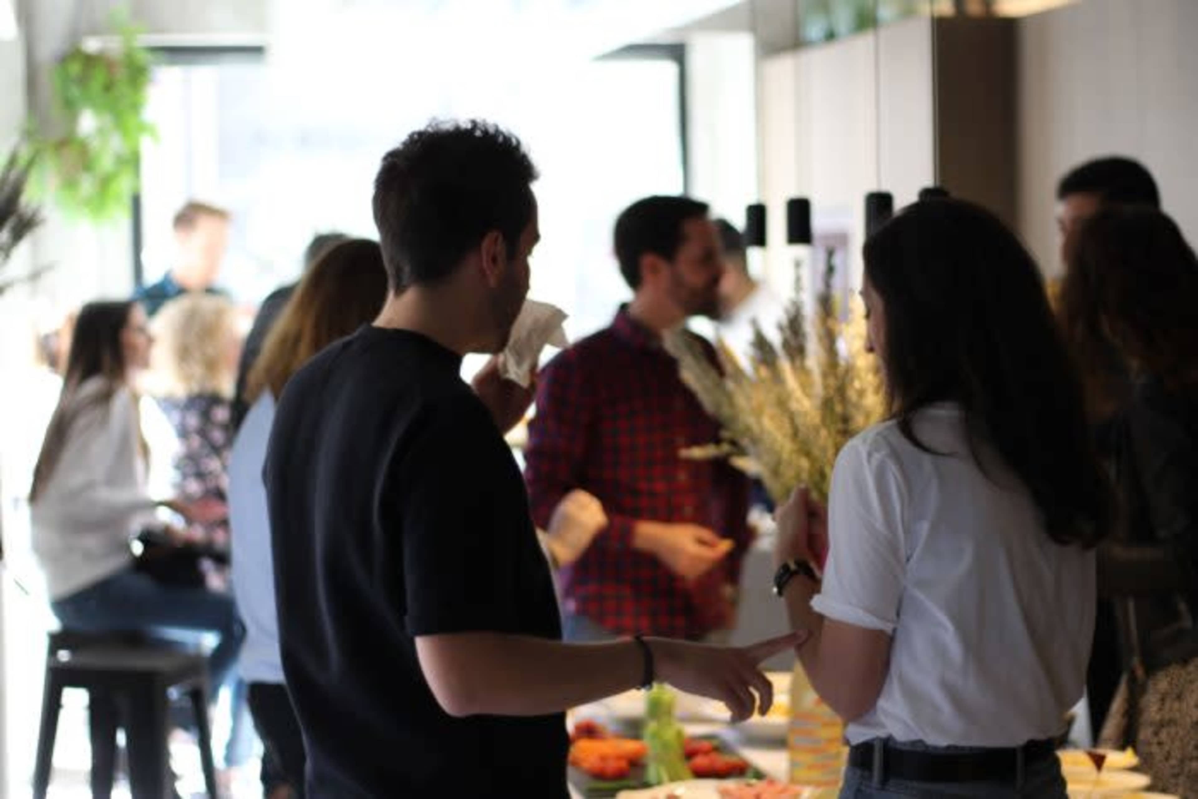 A group of people socialize around a buffet table in a brightly lit indoor setting.