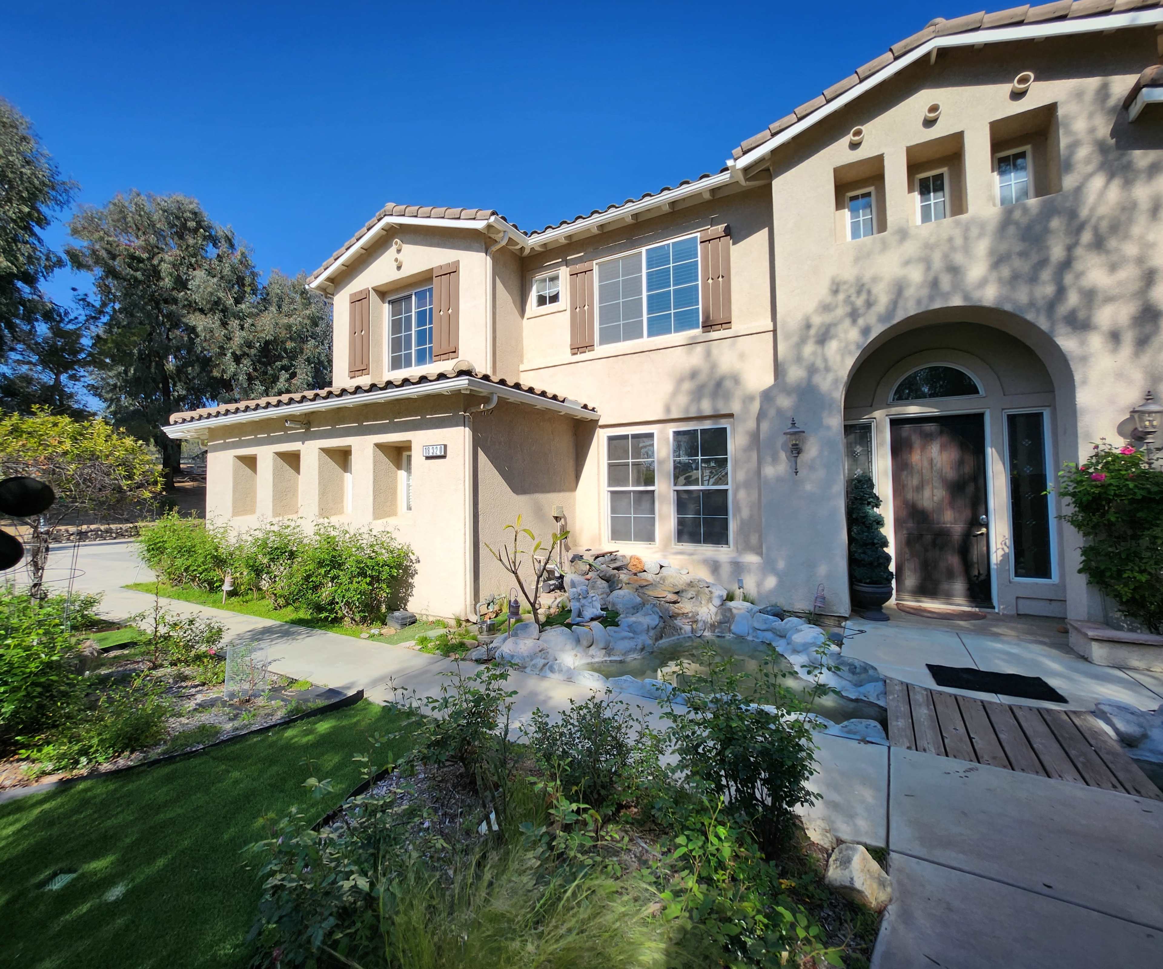 A two-story, stucco house with a landscaped front yard featuring rocks and shrubs.