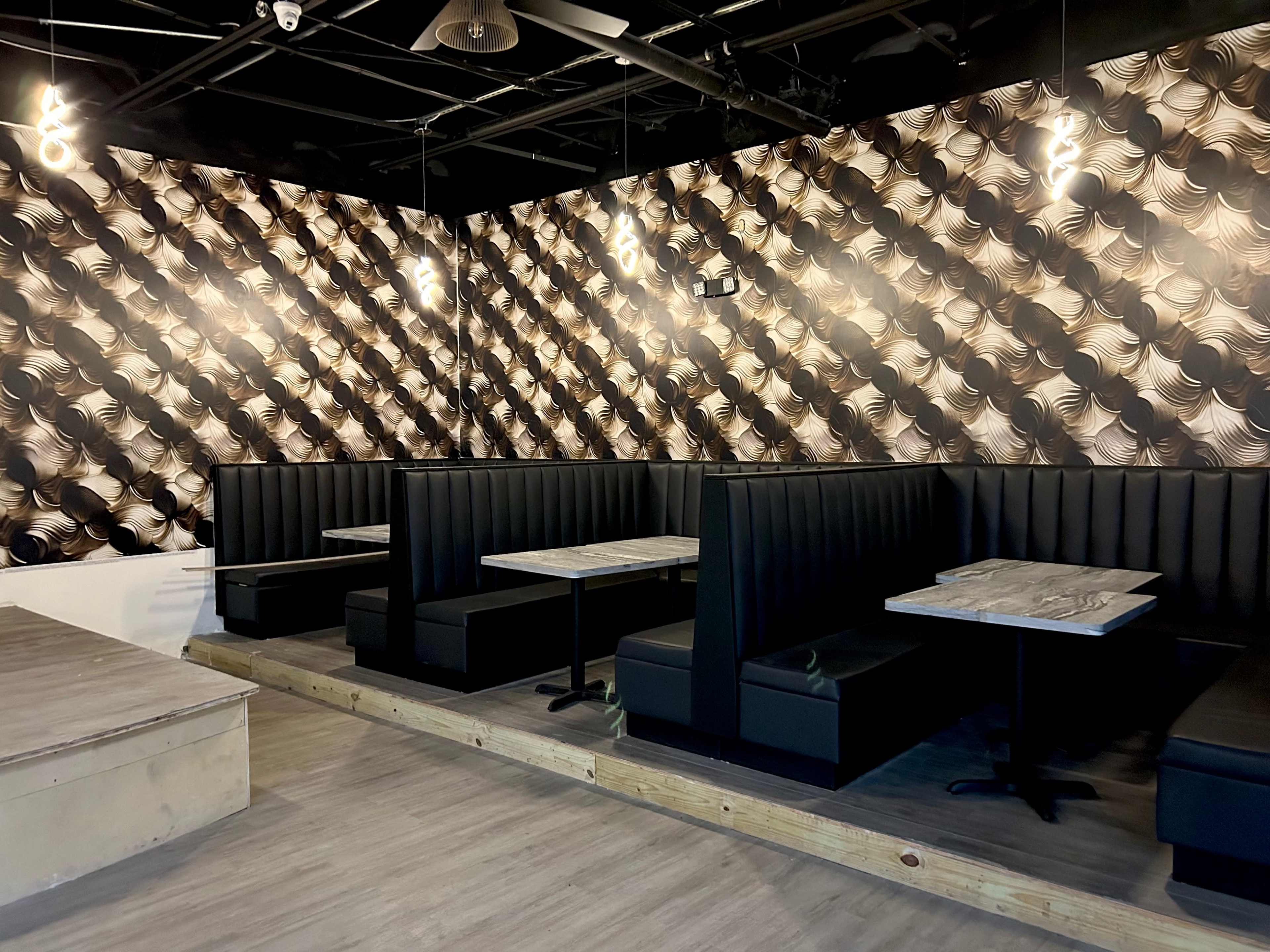 A modern restaurant interior featuring black booth seating with marble-top tables against a patterned wallpaper.