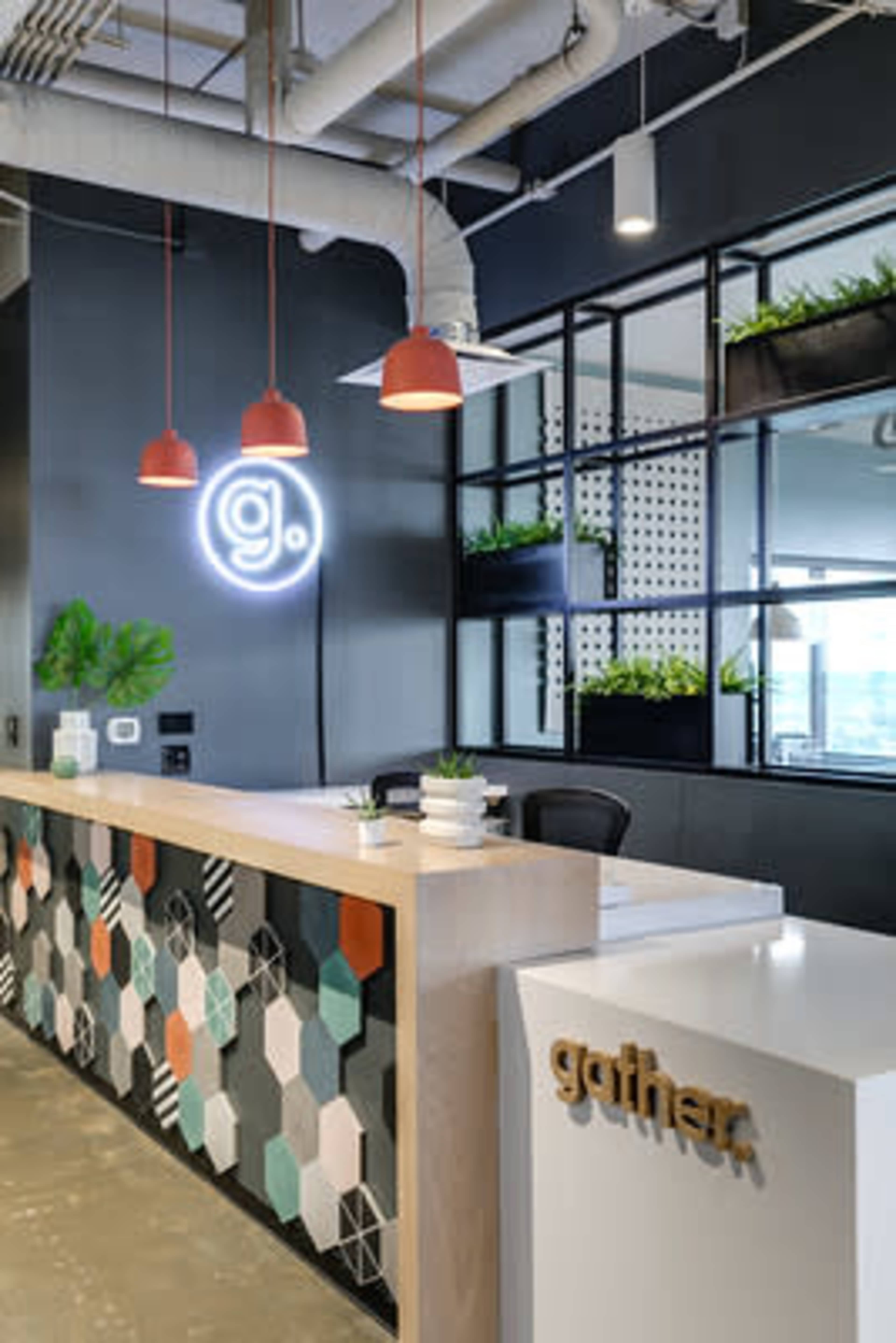 The image shows a modern reception area with a geometric-patterned front desk, decorative plants, and pendant lighting.