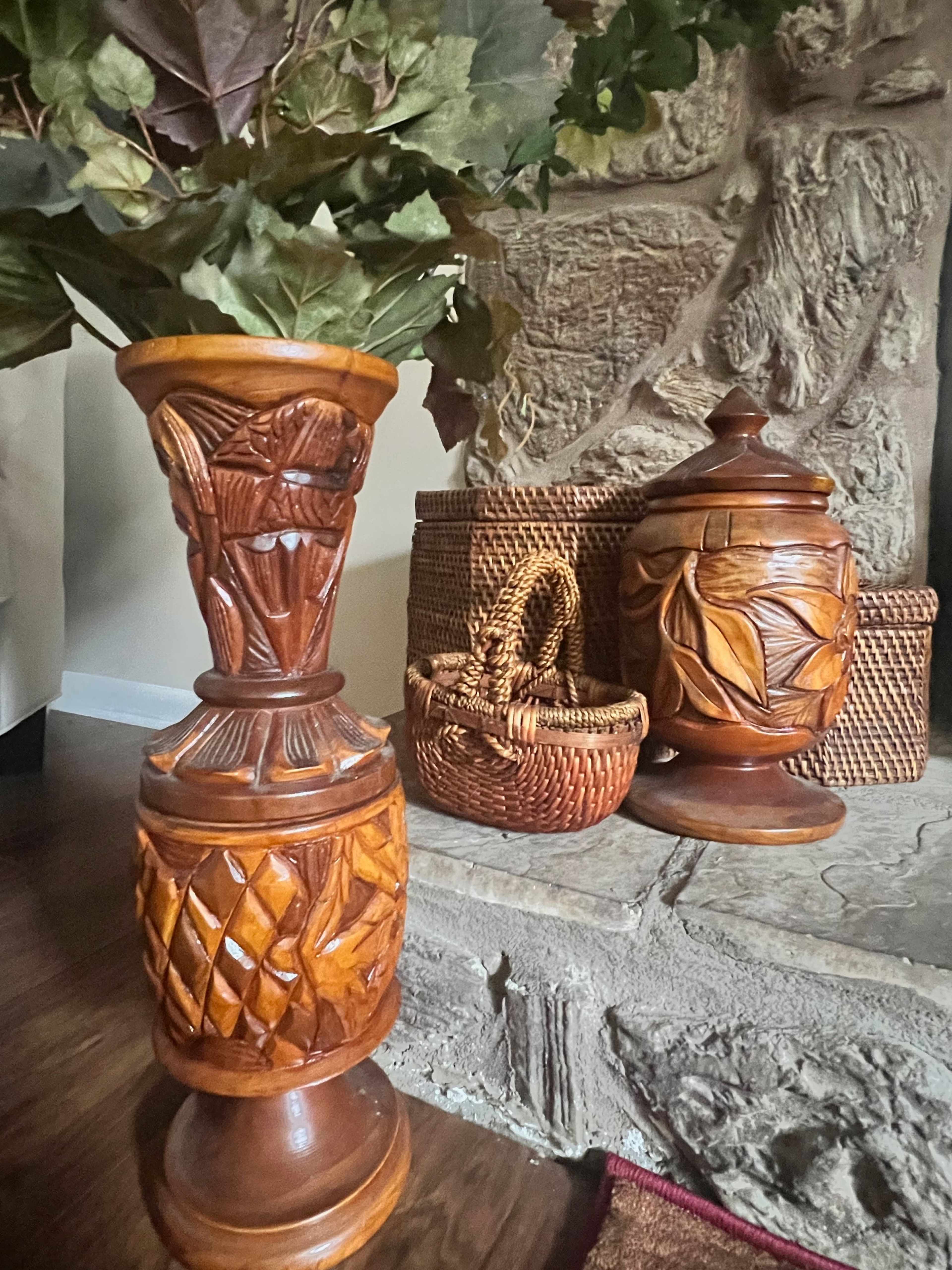 Intricately carved wooden vases and a woven basket placed on a stone surface.